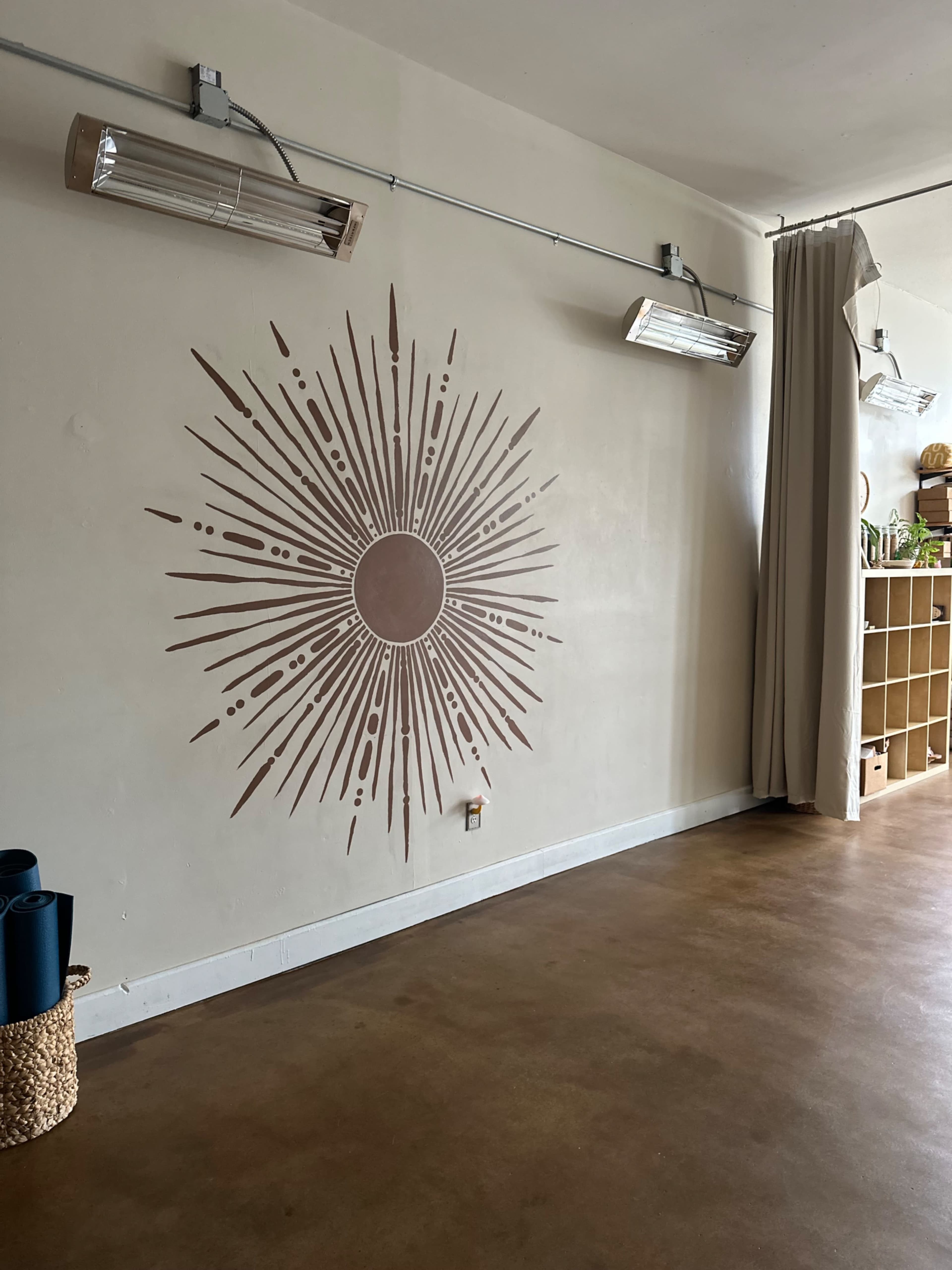 The image shows a minimalist interior space featuring a wall with a sunburst mural and two overhead light fixtures.