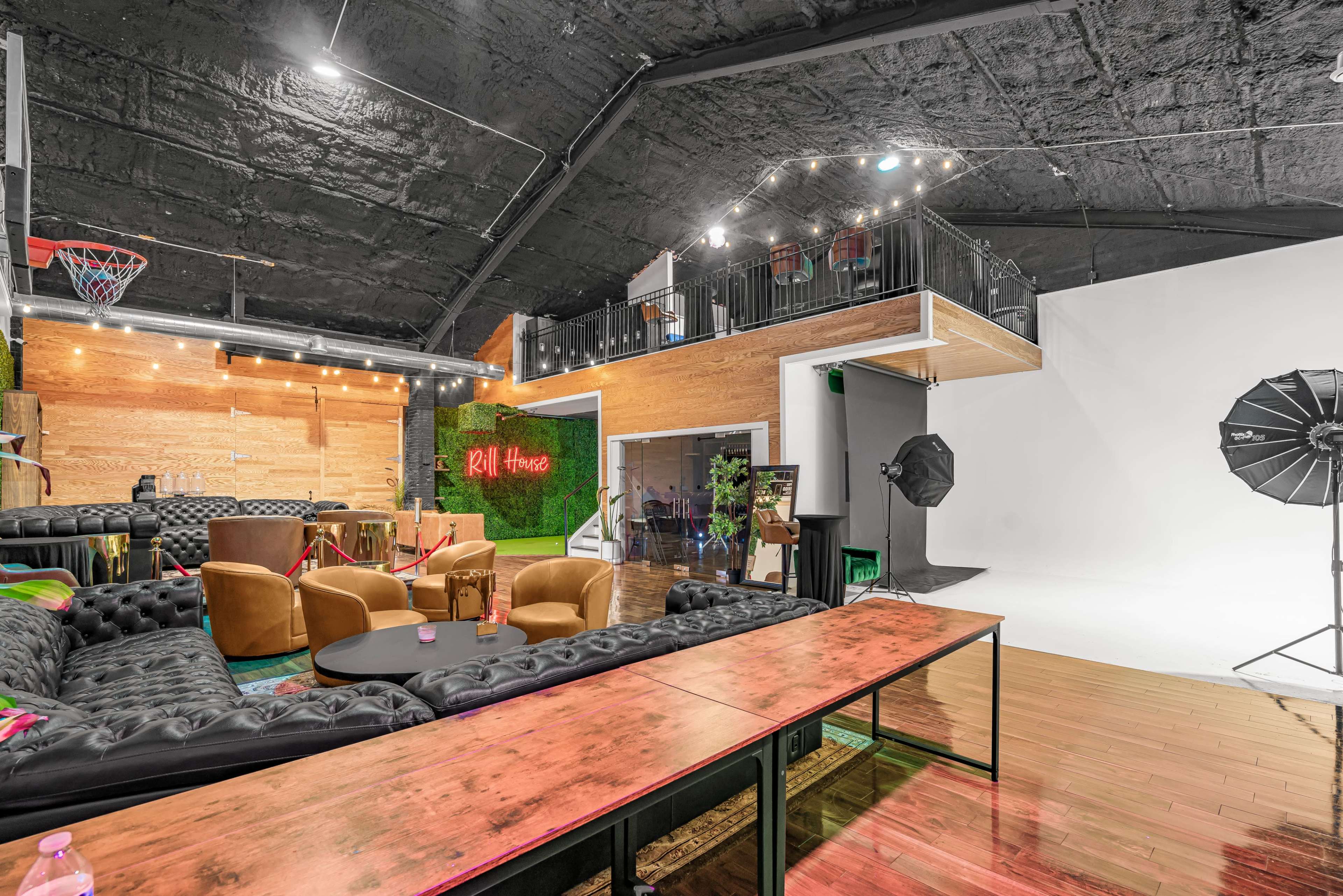 A spacious studio with a lounge area featuring leather seating and a table, alongside a photography backdrop and lighting equipment.