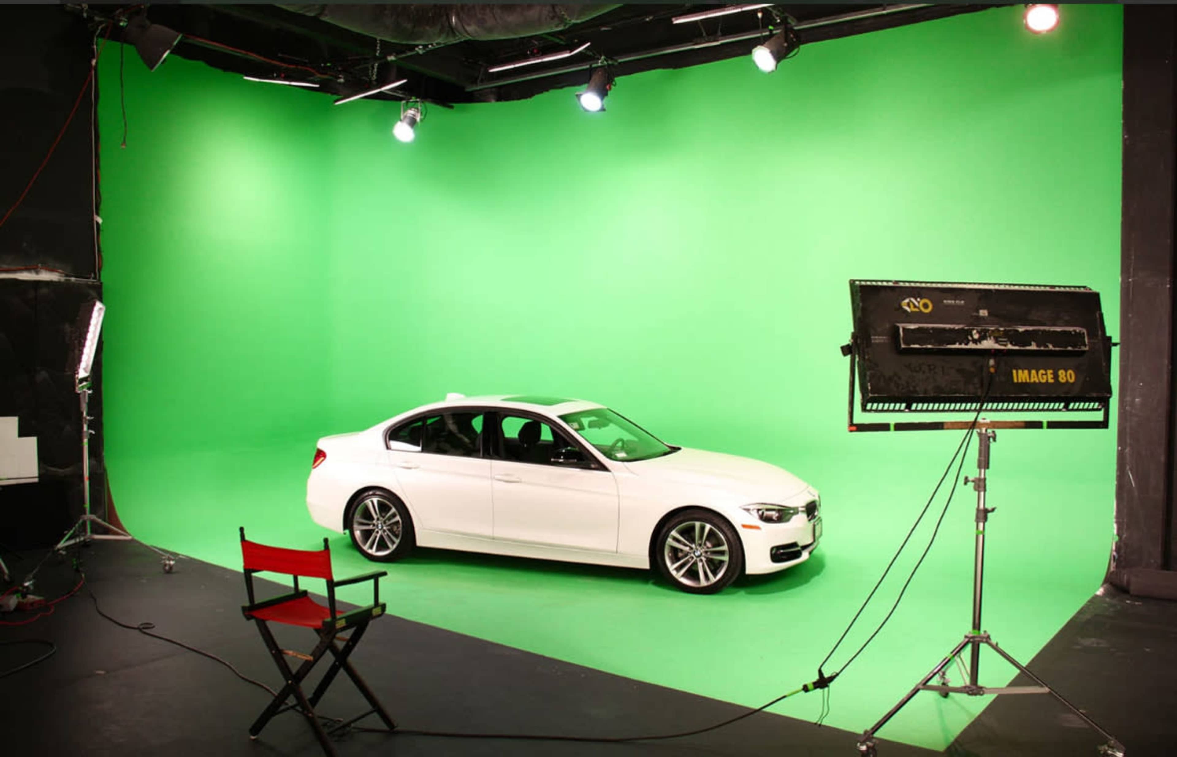 A white car is positioned in front of a green screen in a studio setting.