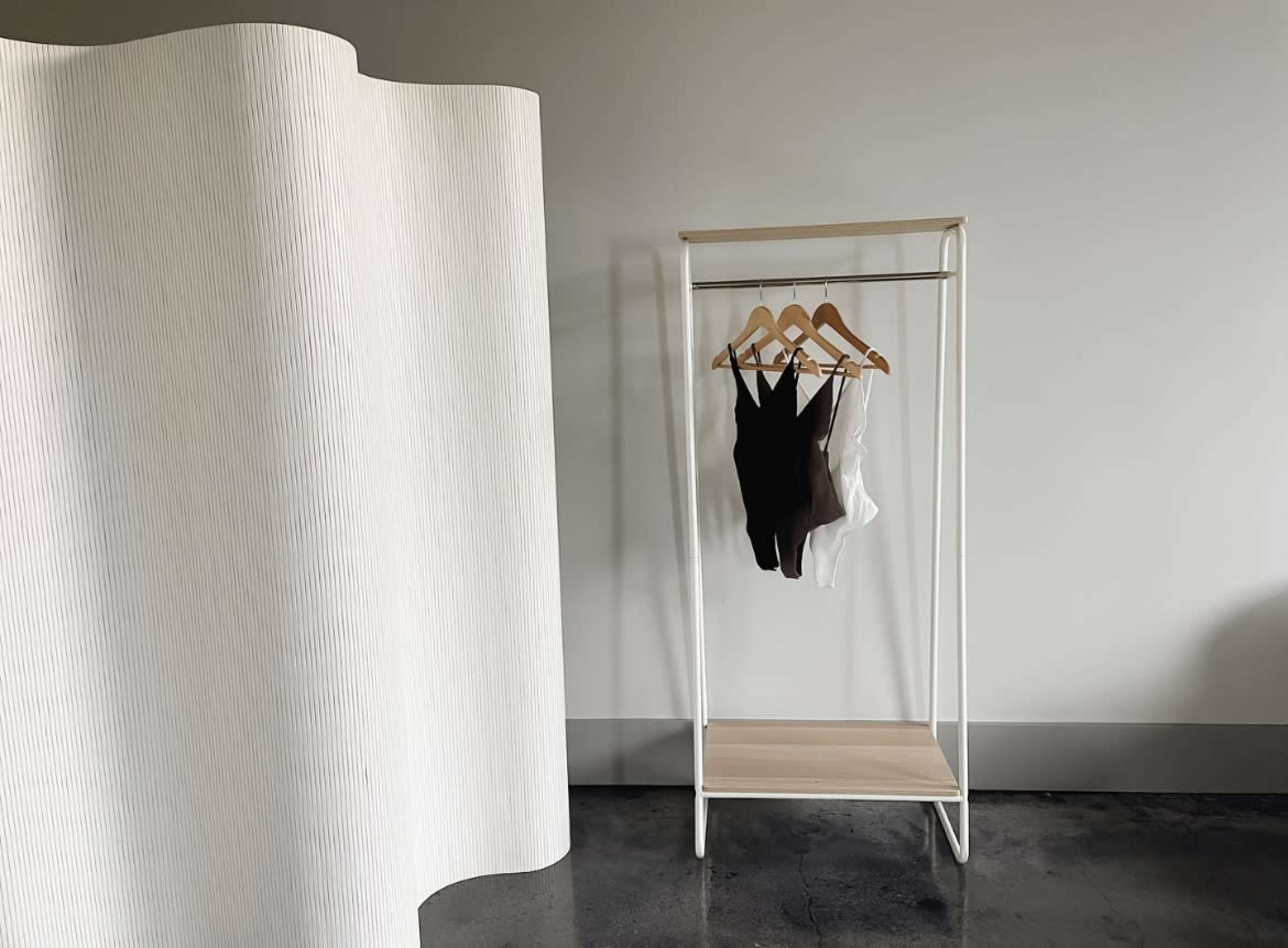 A clothing rack with three items hangs against a plain wall in a minimalist room.