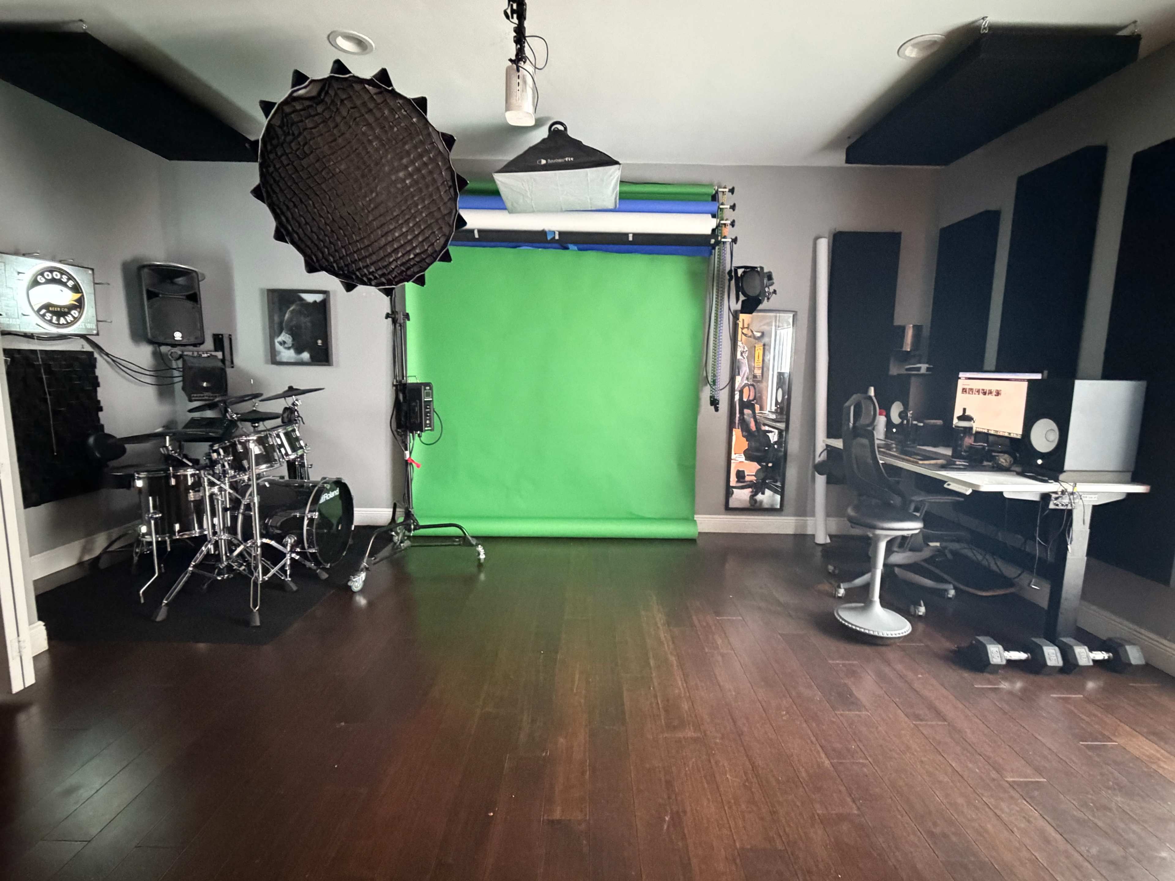 The image shows a music and video production studio featuring a green screen, drum set, and a computer workstation.