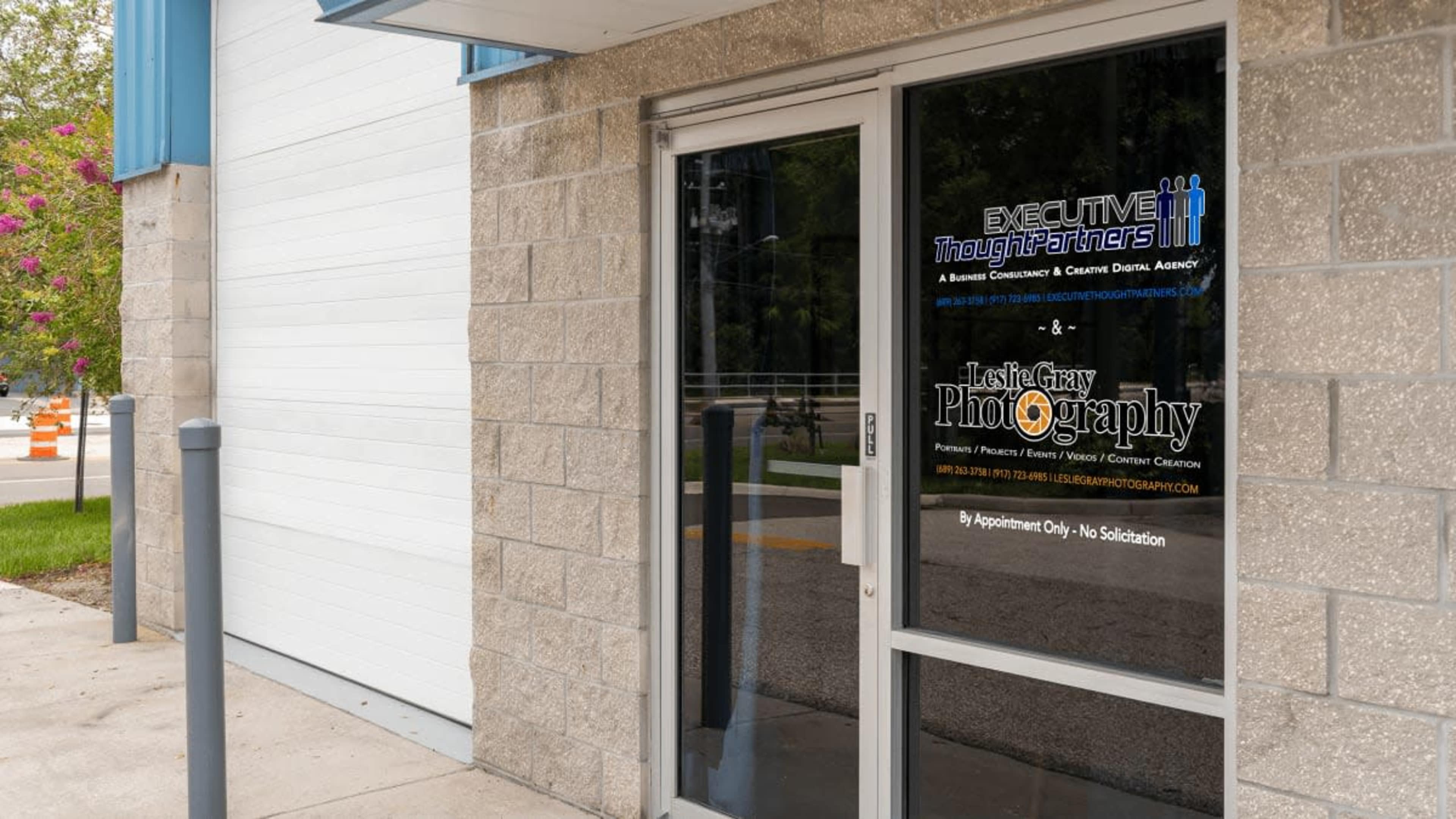 The image shows the entrance of a building featuring a glass door with signage for "Executive Thought Partners" and "Leslie Gray Photography."