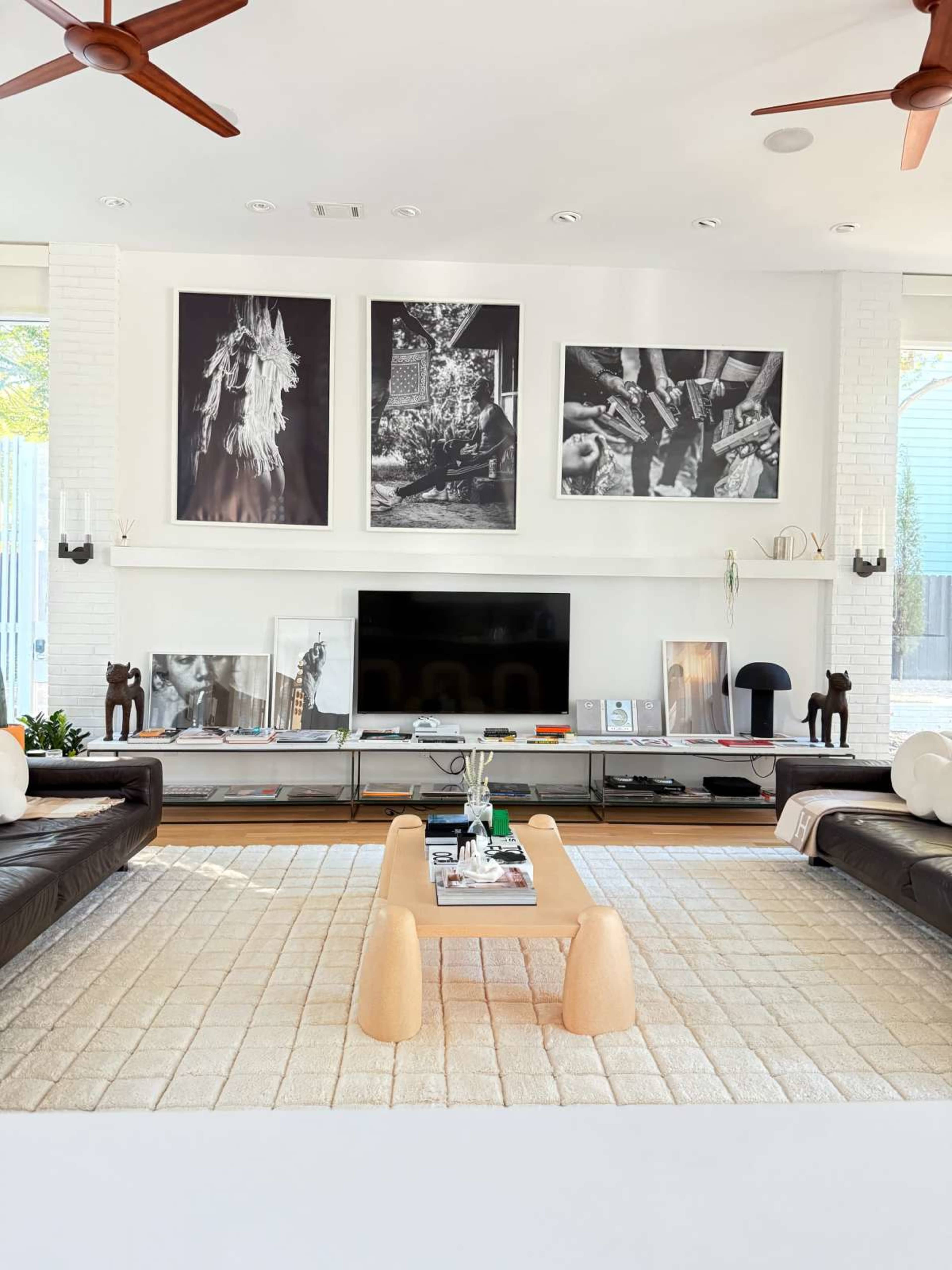 The image depicts a modern living room with a sleek television unit, black and white artwork on the walls, and a light-colored rug beneath a low wooden coffee table.