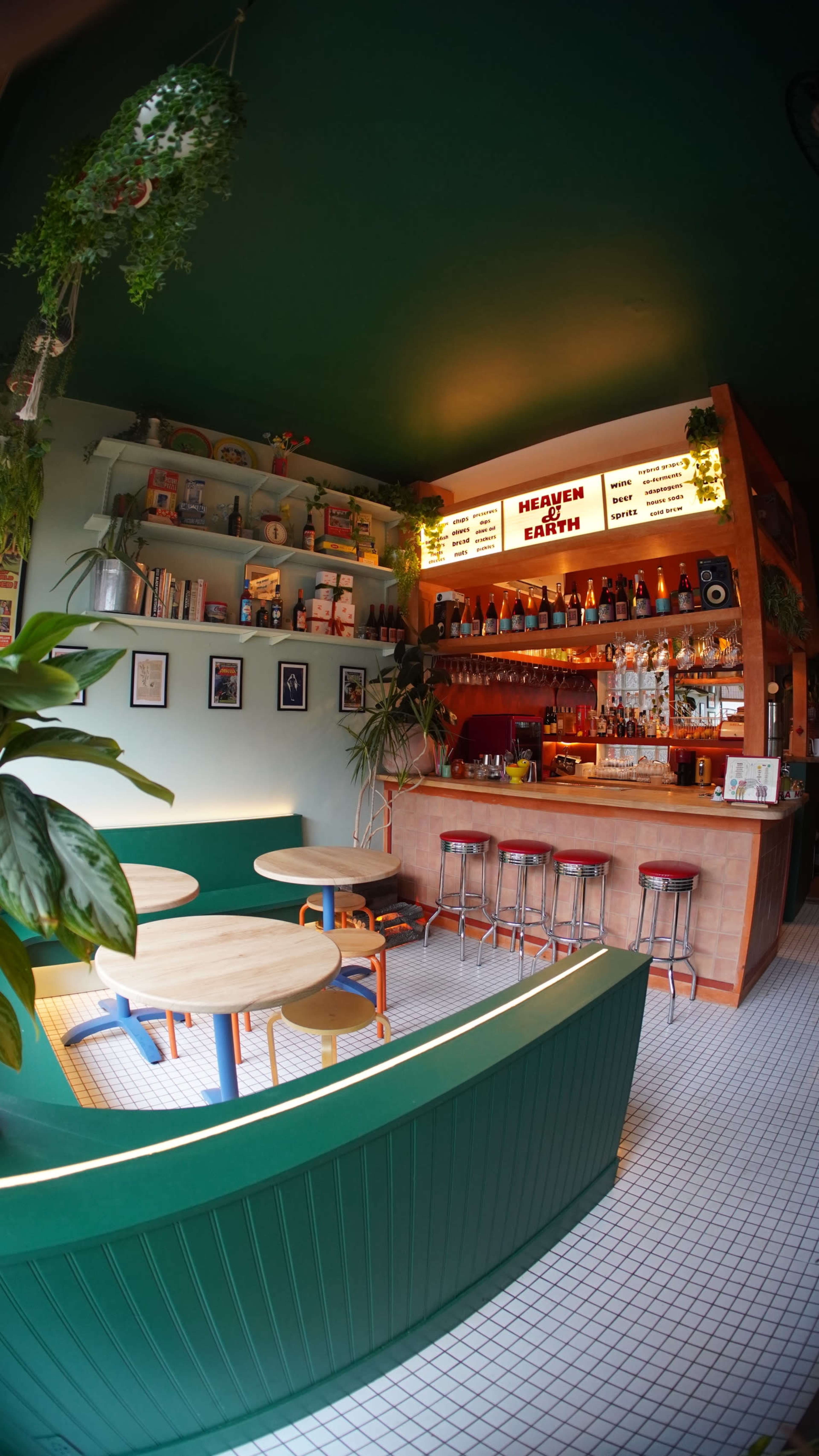 The image shows a cozy bar area with light-colored wood shelves filled with books, plants, and various decorative items, accompanied by a bright green ceiling and colorful bar signage.