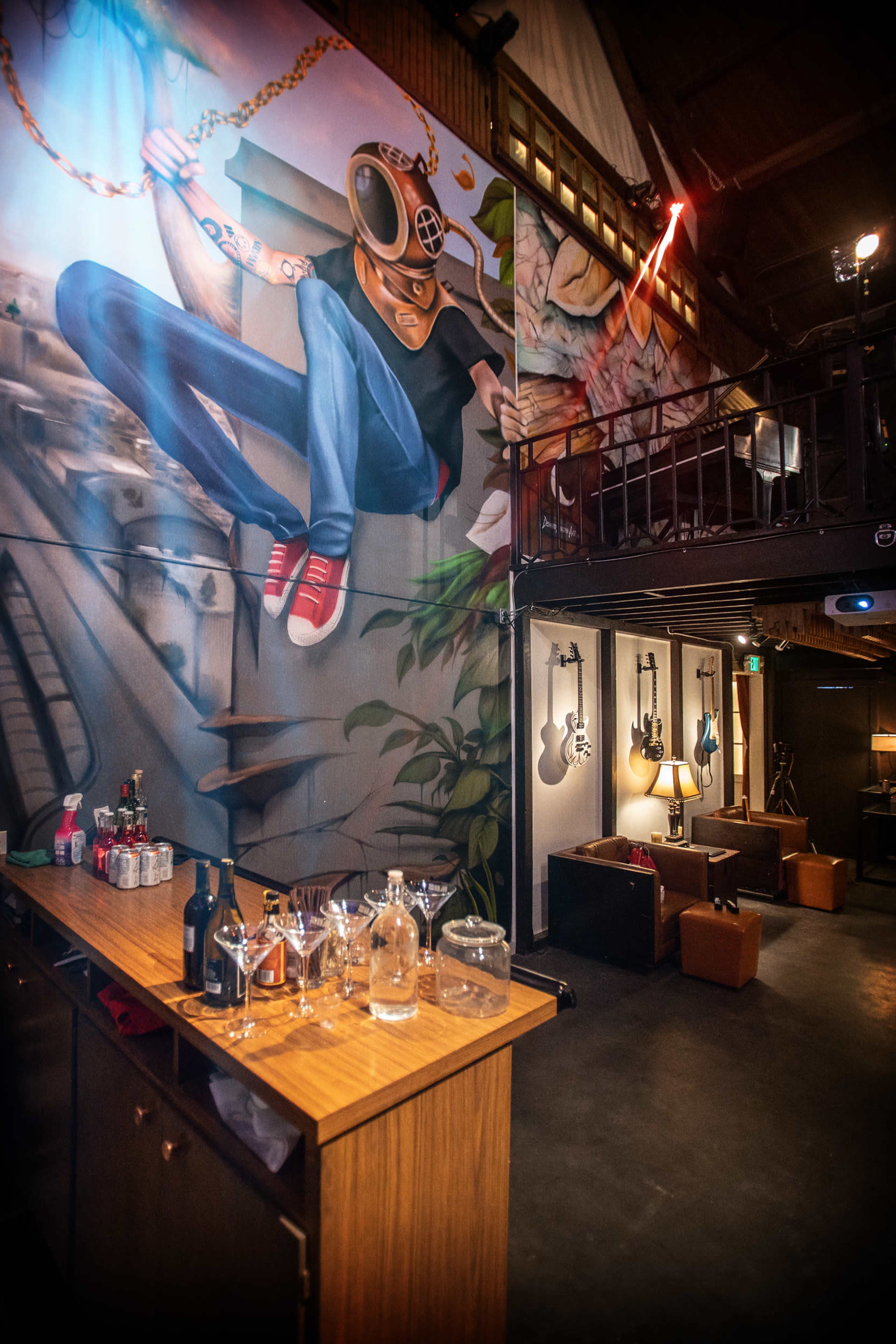 The scene features a bar area with a wooden counter displaying various bottles and glasses, alongside a colorful mural of a figure in a helmet, and a wall adorned with guitars in a dimly lit venue.