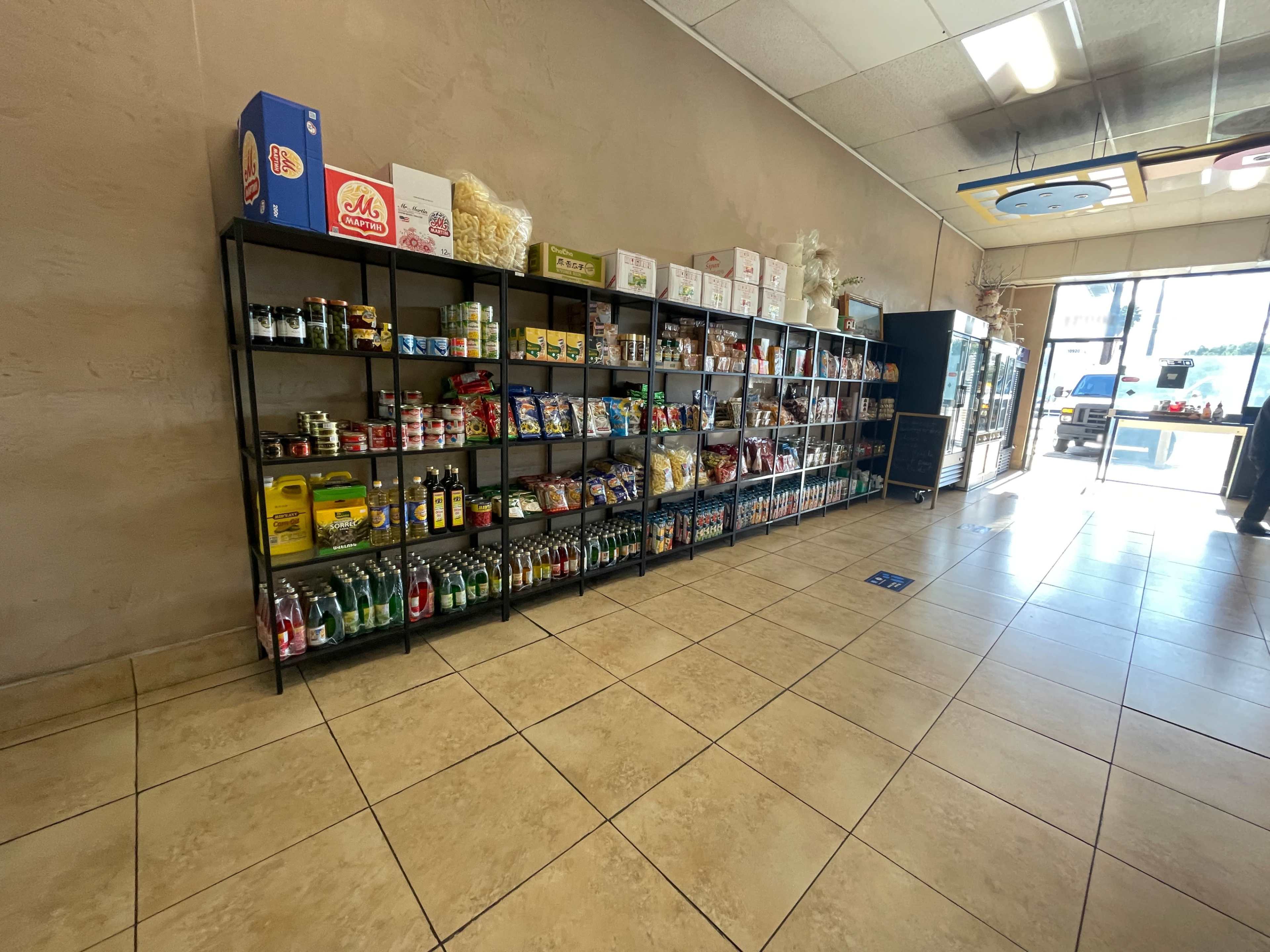 A row of shelves stocked with various canned goods, beverages, and snacks lines a wall in a grocery store.