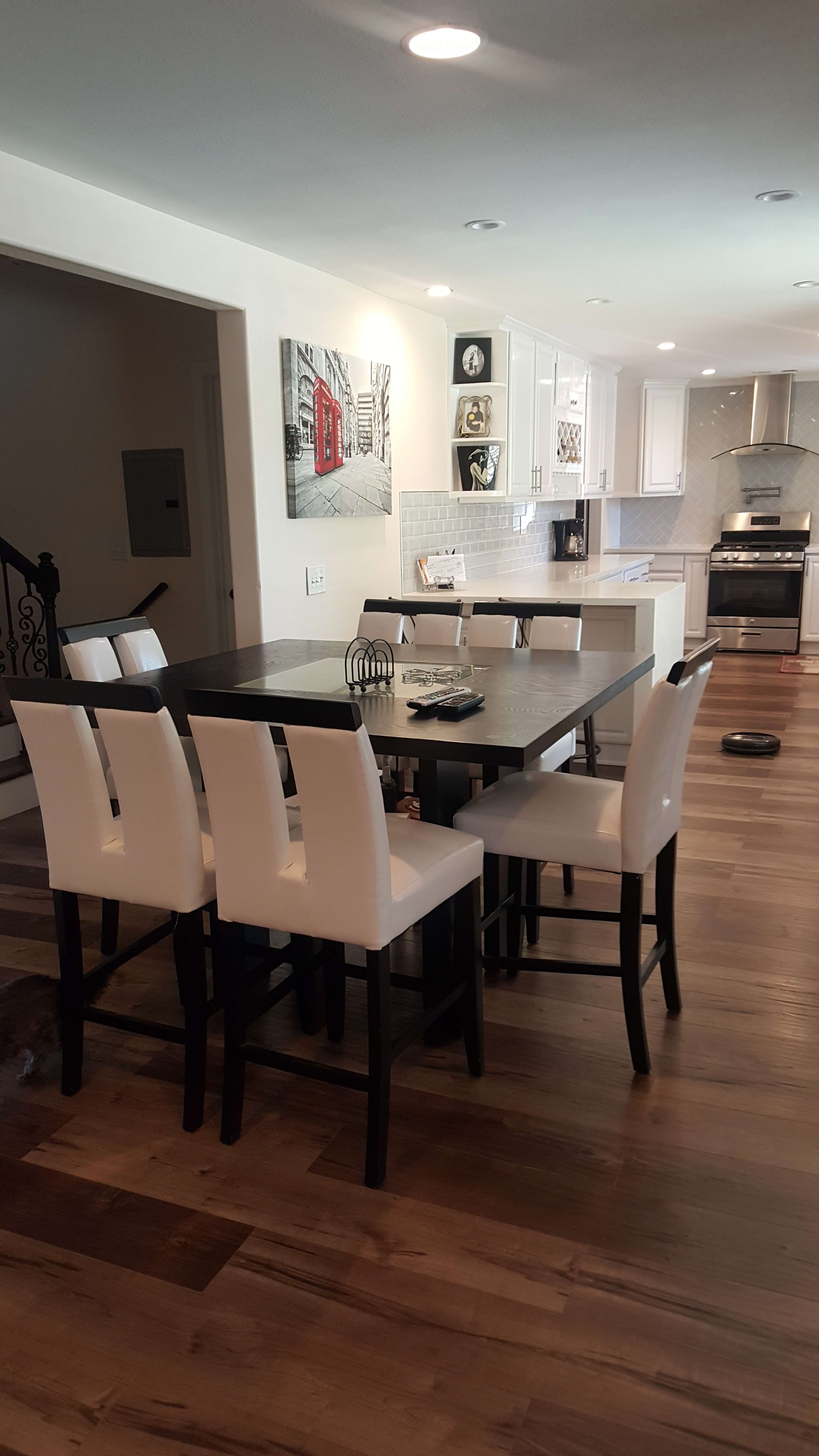 A modern kitchen features a central island with a dark table surrounded by white chairs, and stainless steel appliances in the background.