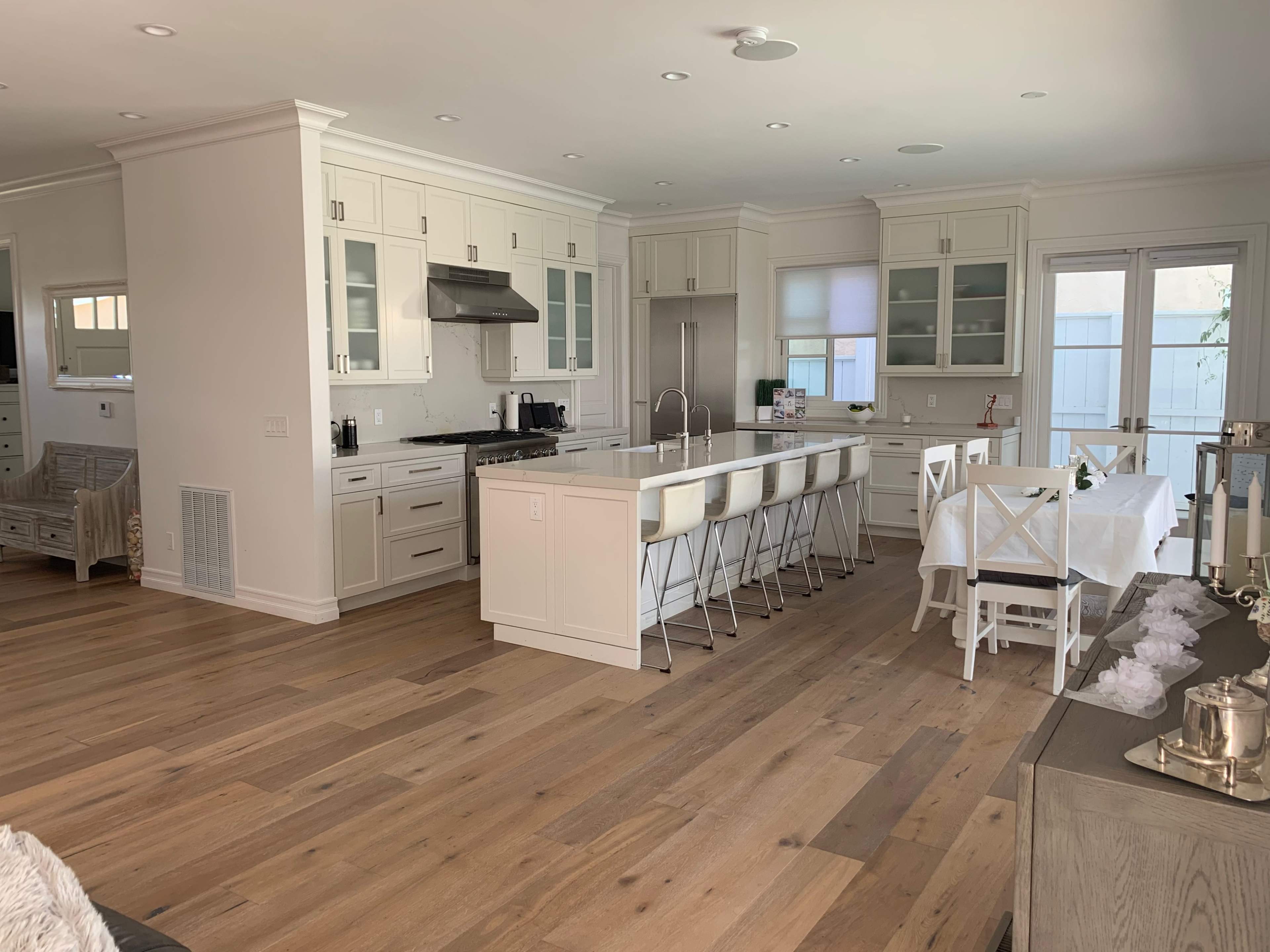 The image shows a modern kitchen and dining area with a large island, white cabinetry, and a dining table set for several people.