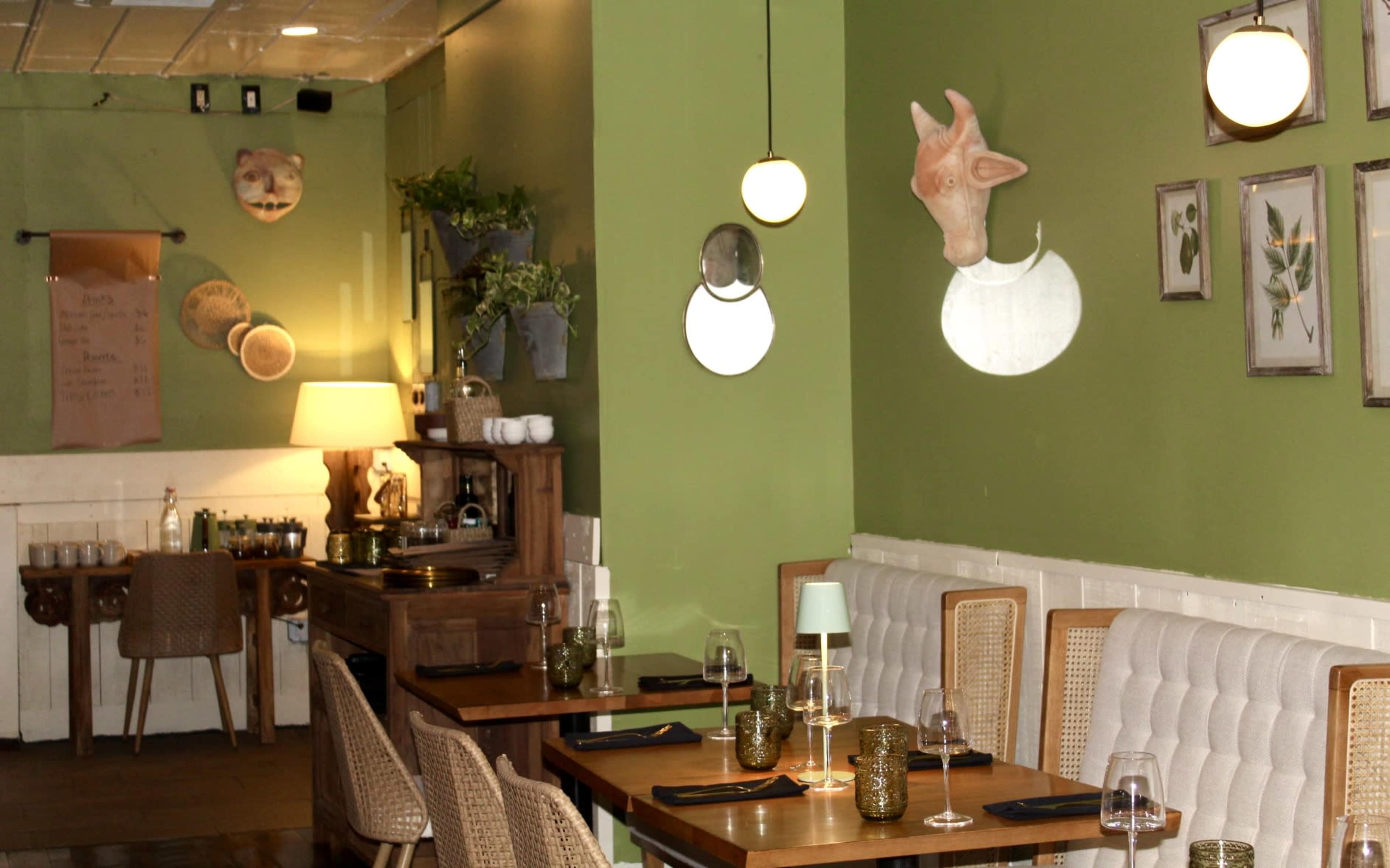 The image shows a restaurant interior with green walls, wooden tables, and decorative animal heads mounted on the wall.
