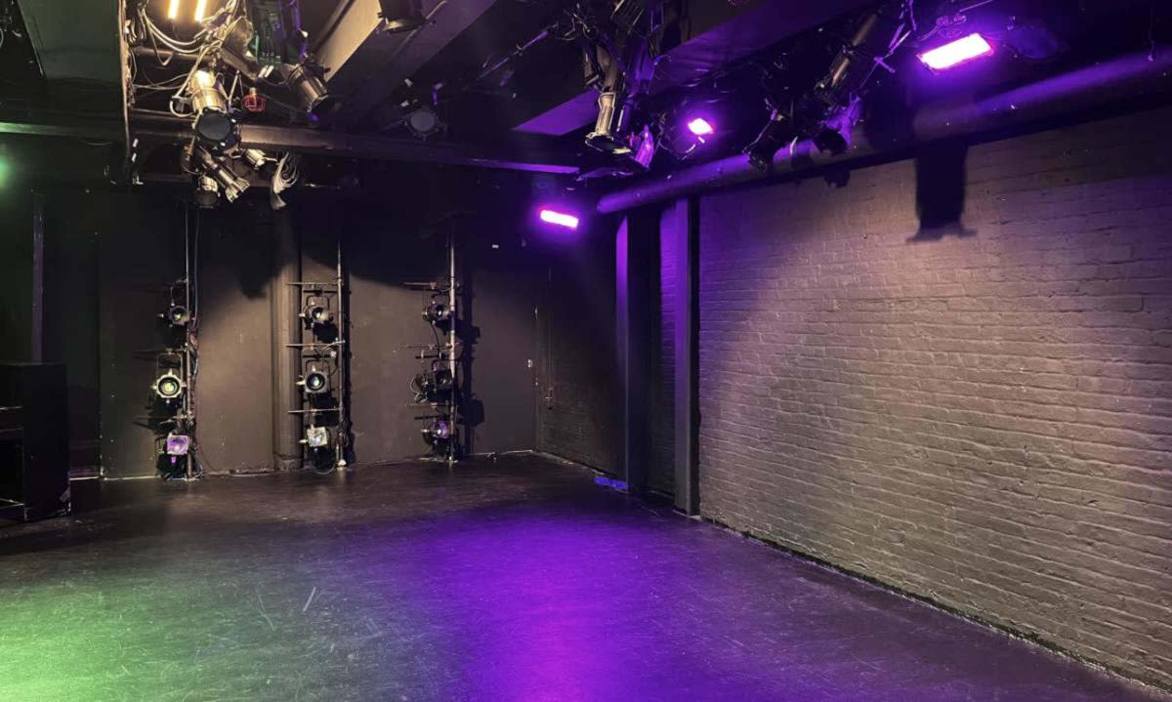 The image shows a dimly lit stage with black walls and several lighting fixtures mounted on the ceiling and side walls.