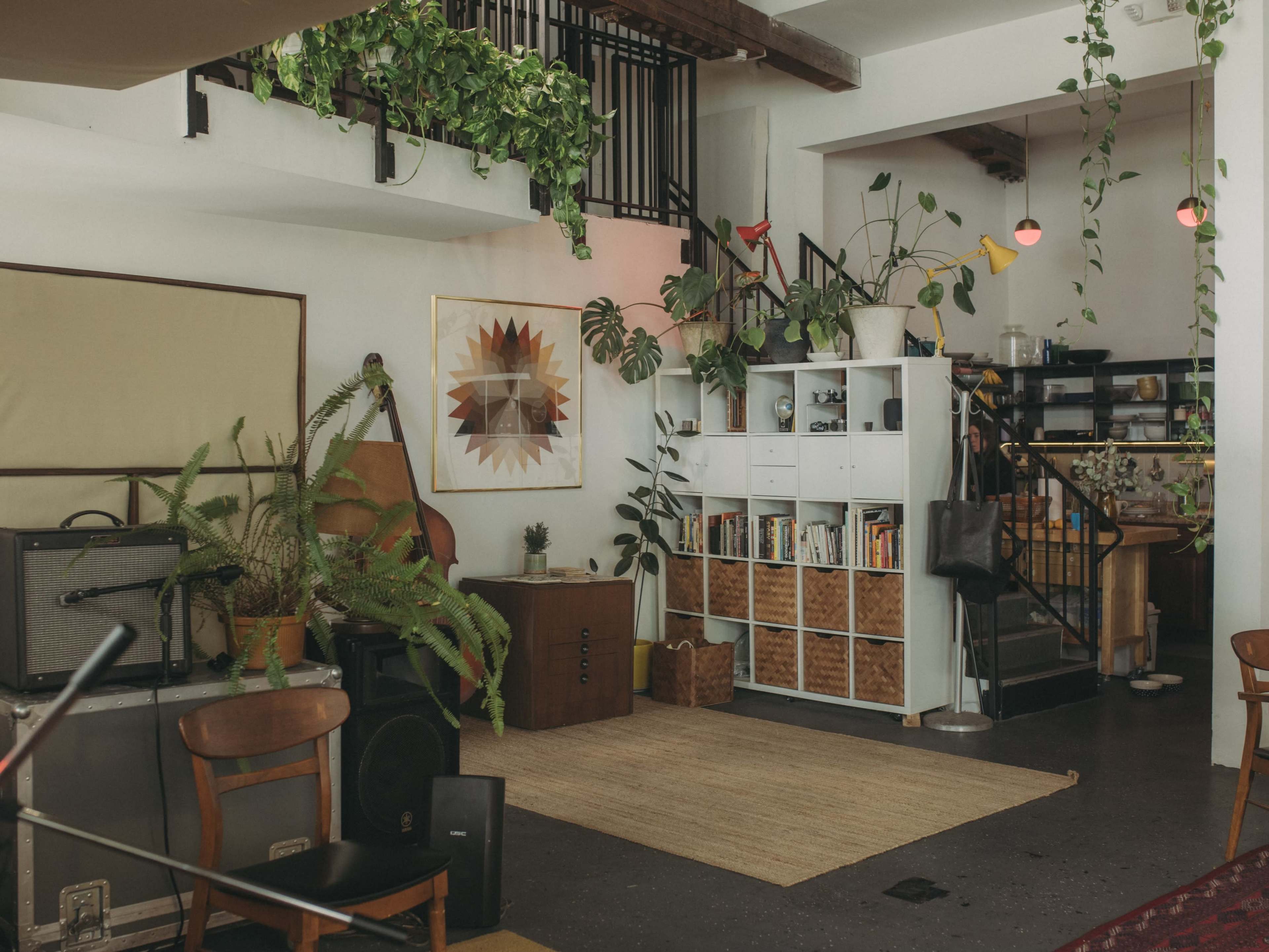 The image showcases a modern living space with indoor plants, bookshelves, and a staircase leading to an upper level.