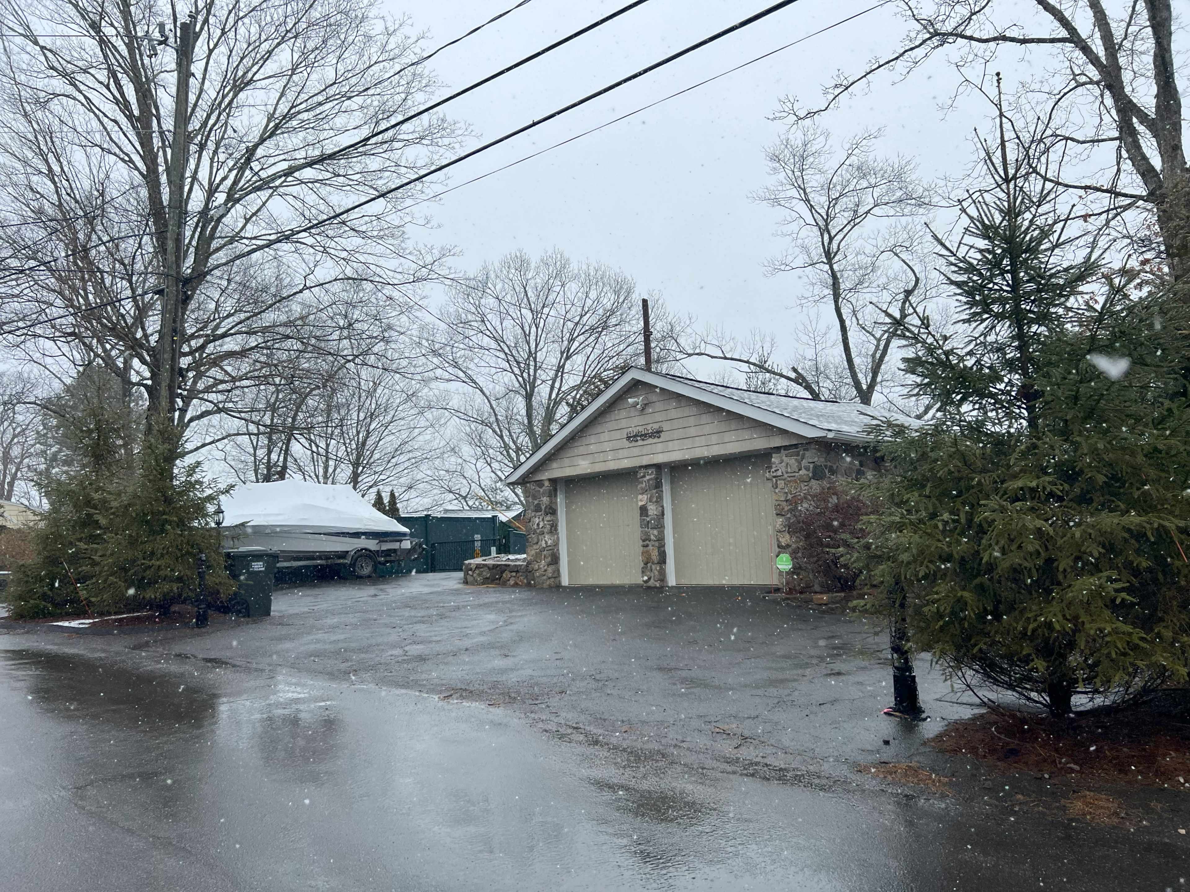 A garage with a stone facade is visible on a rainy day, surrounded by bare trees and a covered boat nearby.