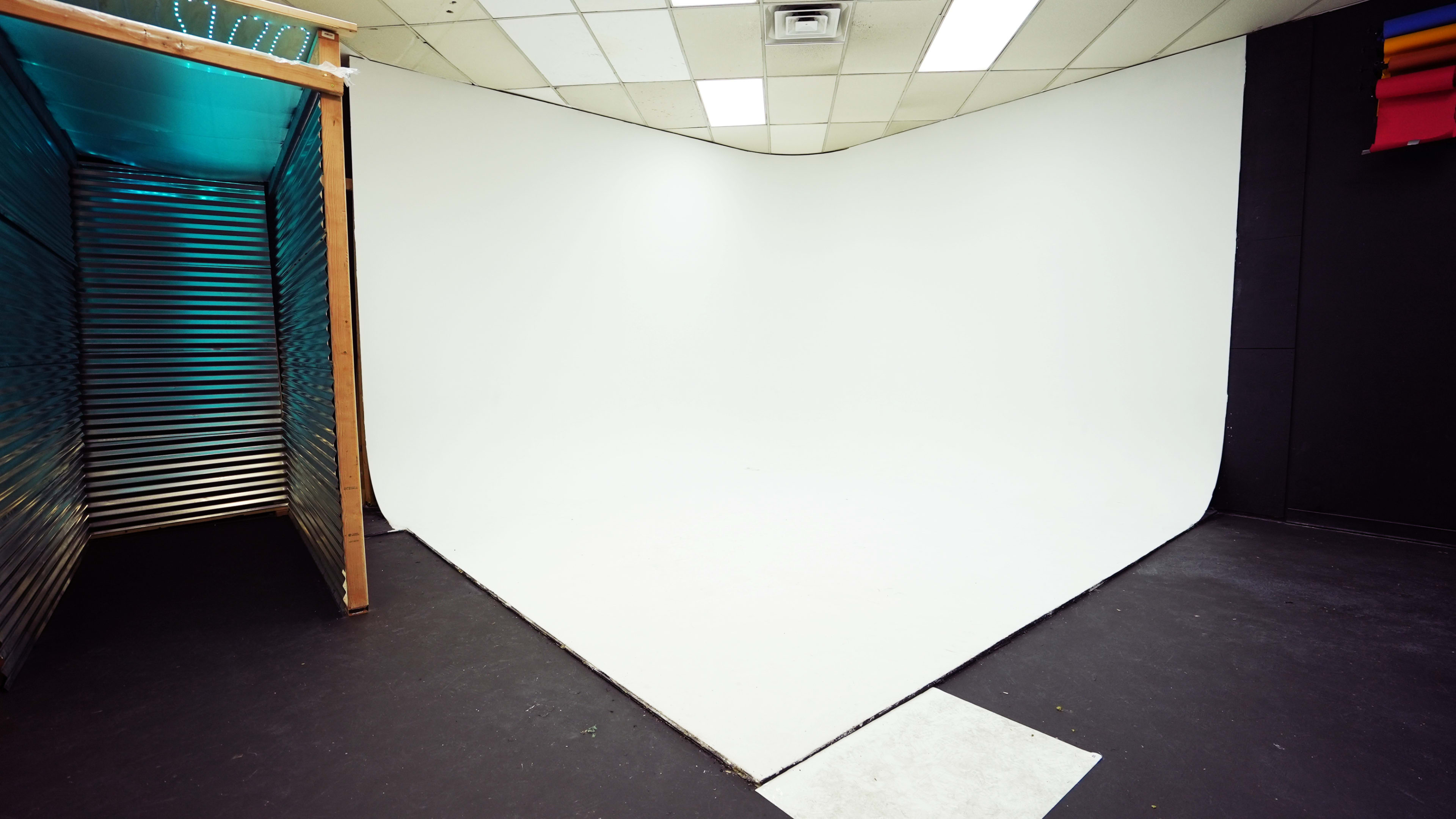 A photography studio with a seamless white backdrop and a corner entrance made of wood and metal.