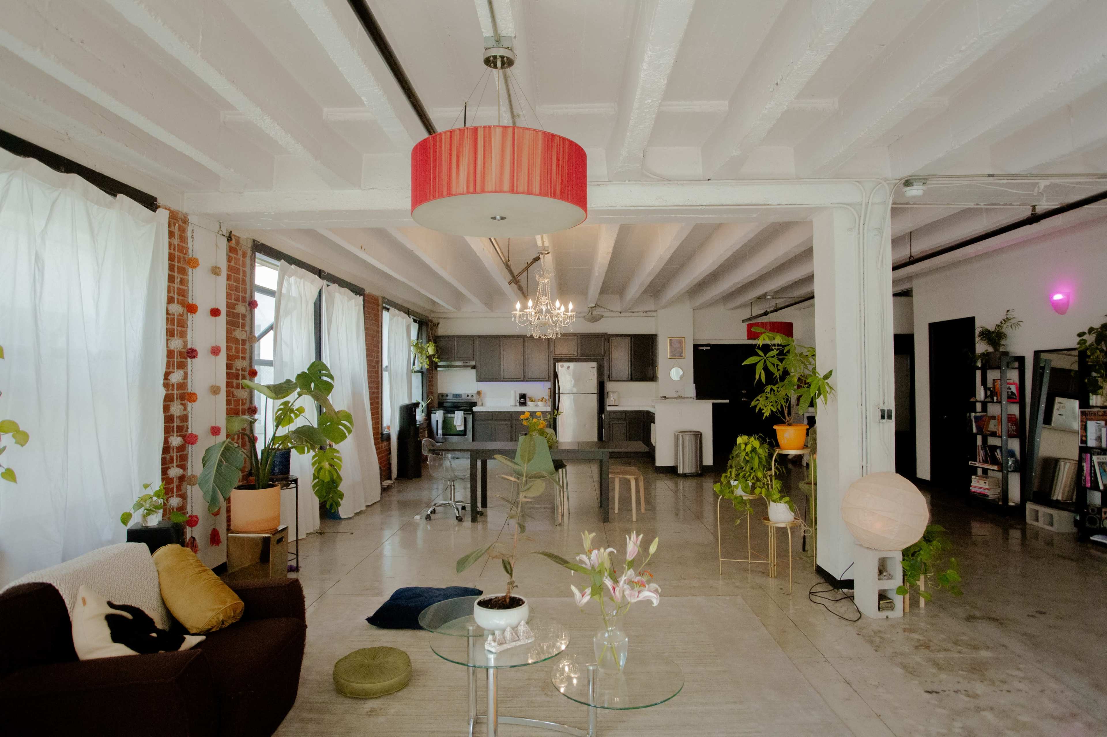 A spacious, modern loft features exposed beams, large windows, and contemporary furnishings, with plants and decorative elements throughout the room.