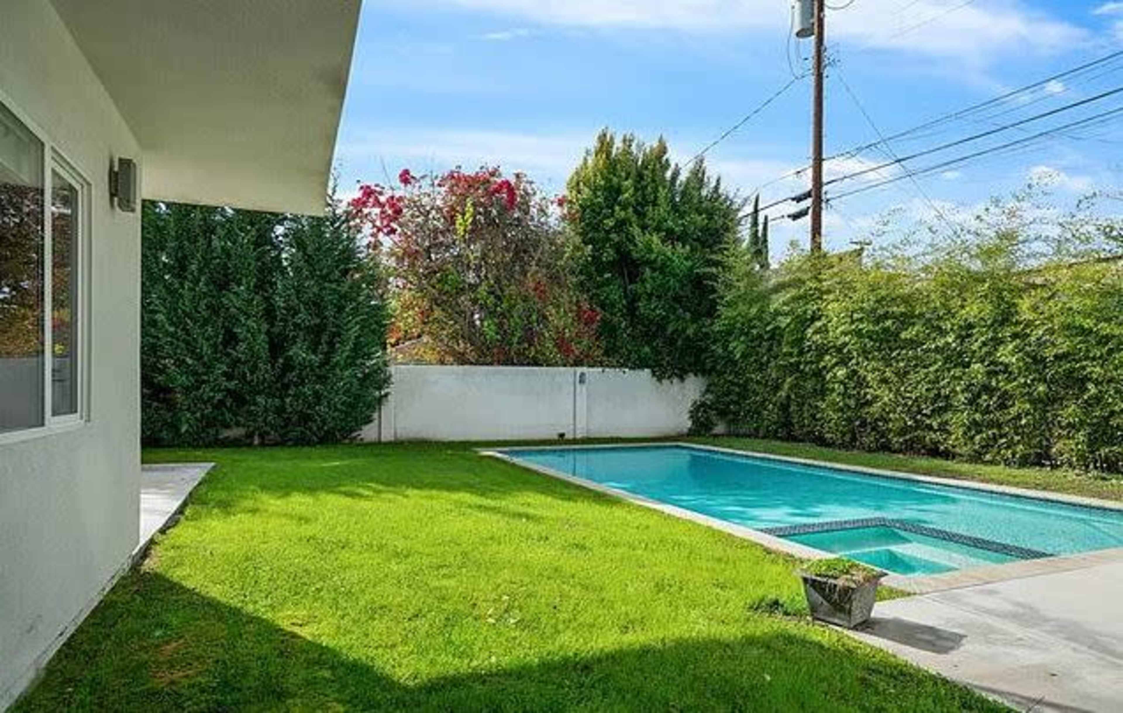 A backyard with a swimming pool surrounded by grass and trees, with a clear sky in the background.