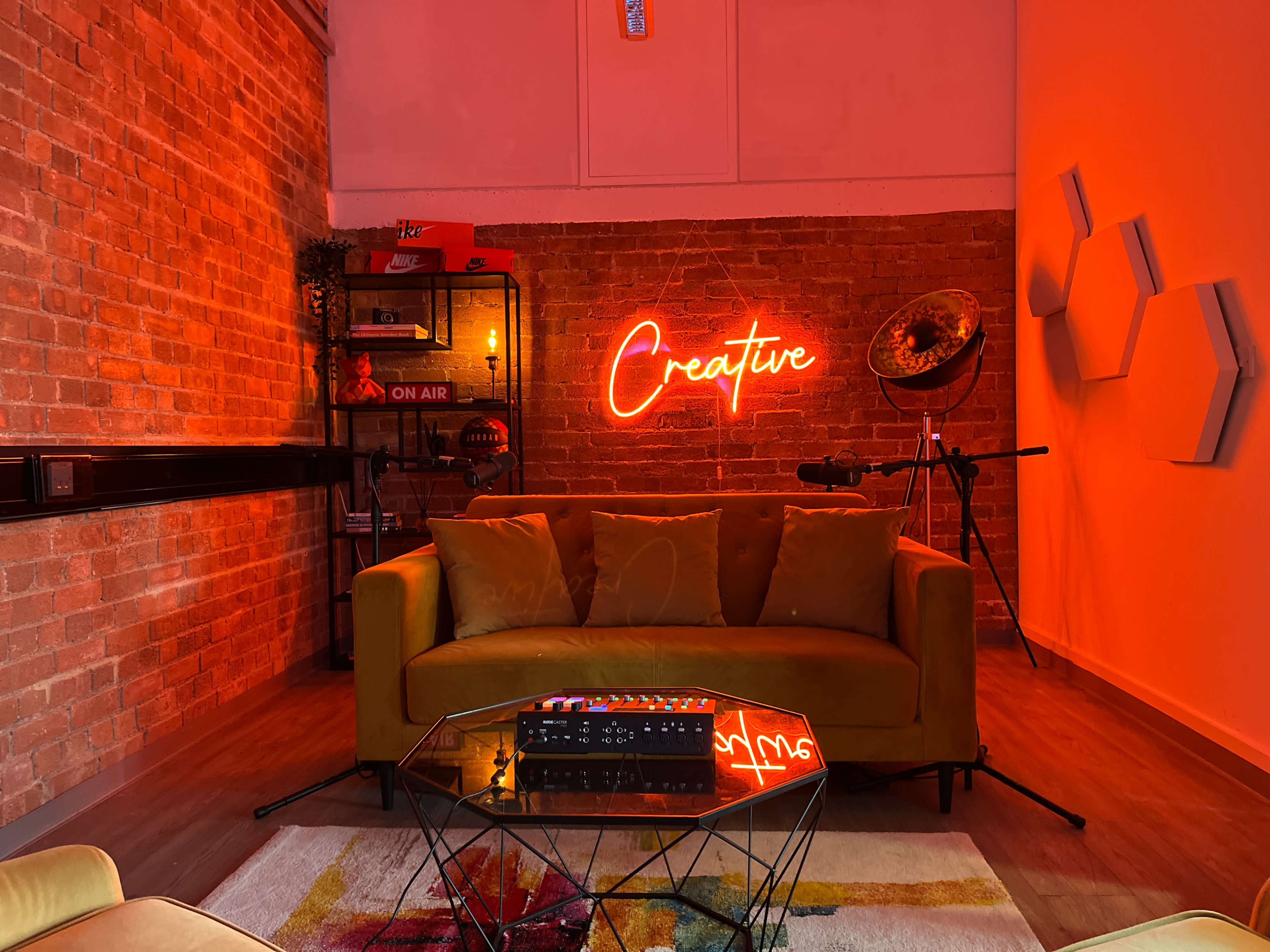 A cozy, modern living space featuring a yellow sofa, a glass coffee table, and a neon sign that reads "Creative" against a brick wall.