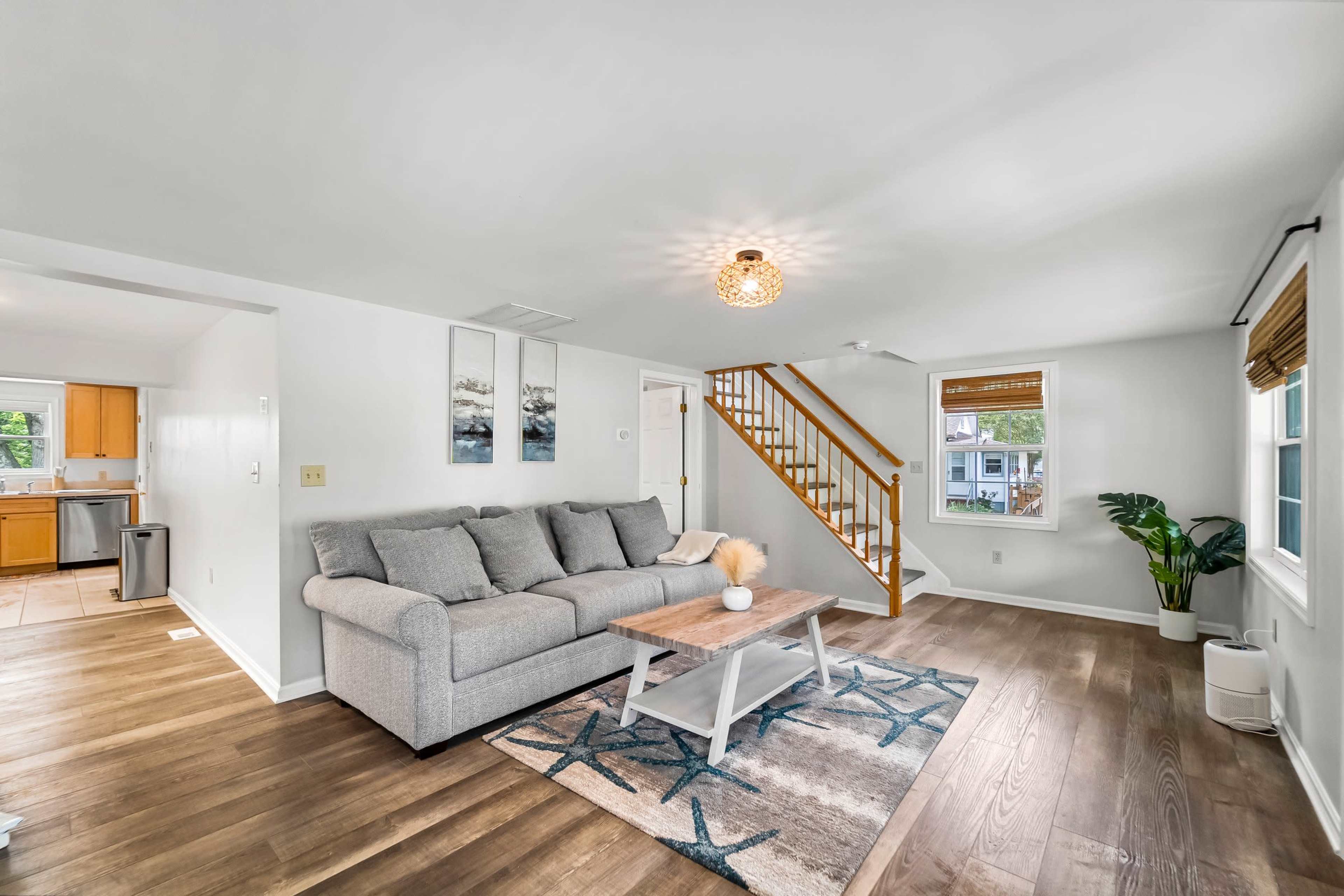 The living room features a gray sofa, a coffee table on a patterned rug, and a staircase leading to the upper level.