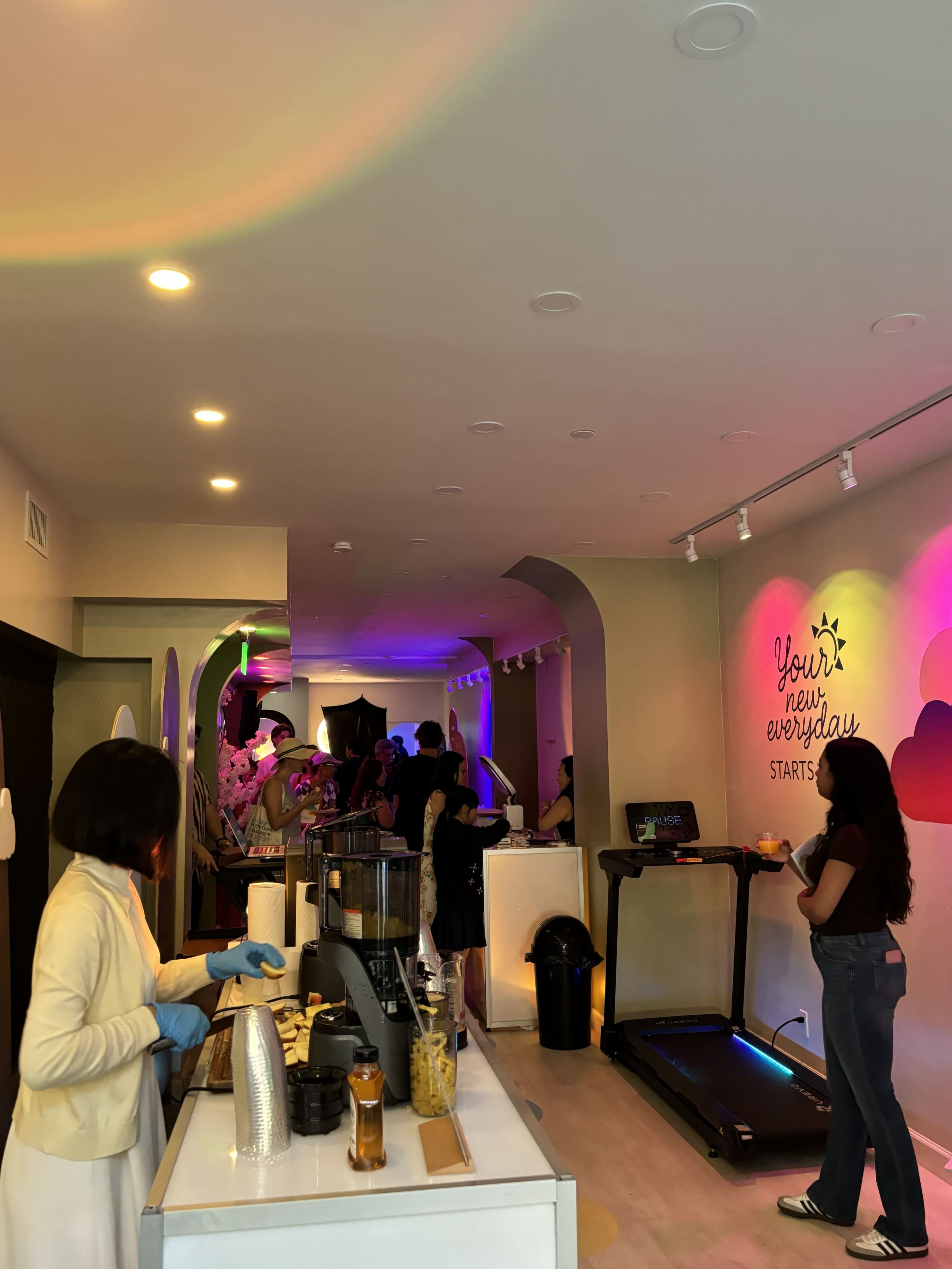 The image shows a lively indoor space with people socializing, a coffee bar setup on the left, and colorful lighting enhancing the atmosphere.