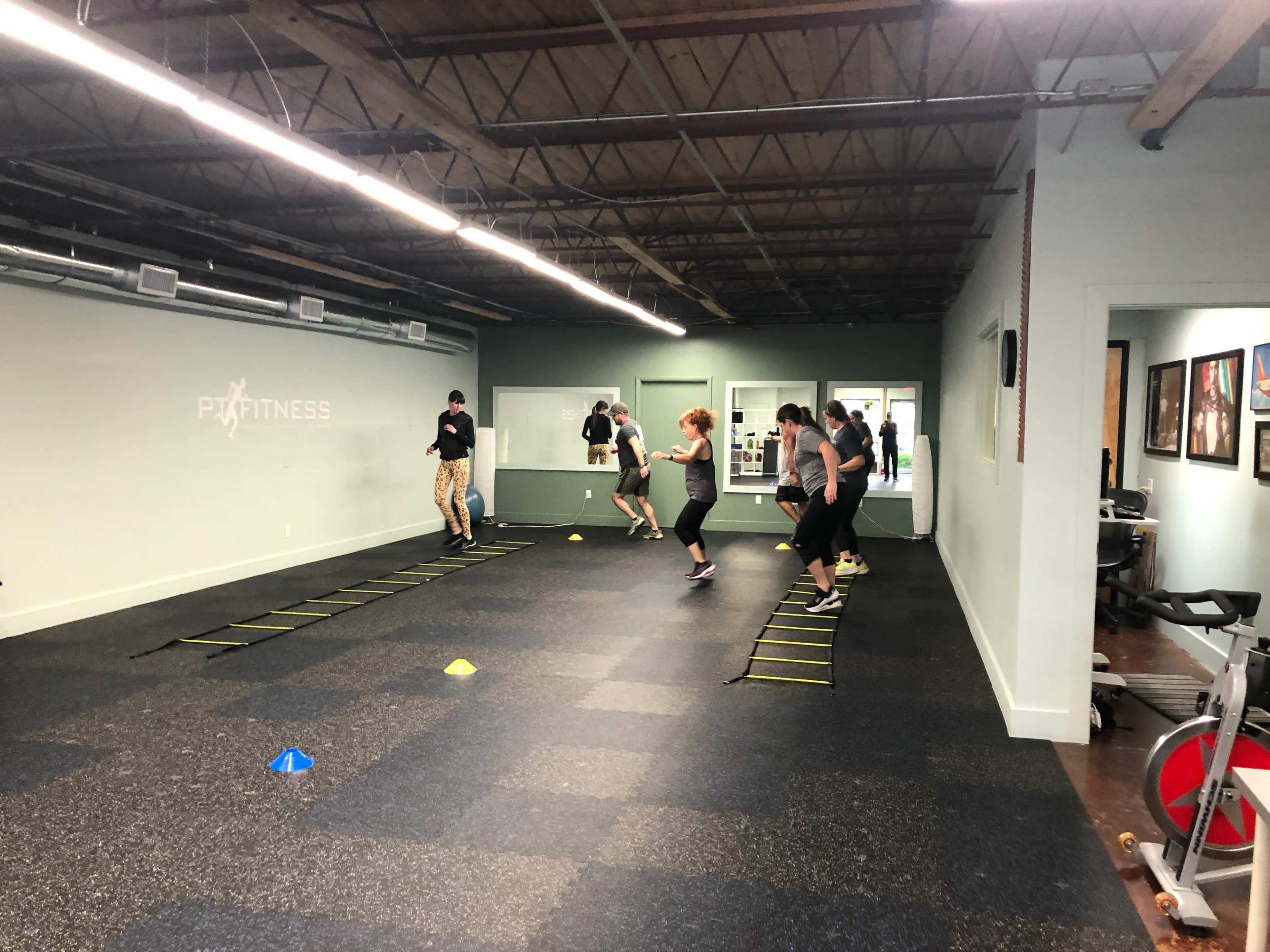 A group of people is exercising on agility ladders and cones in a fitness facility.