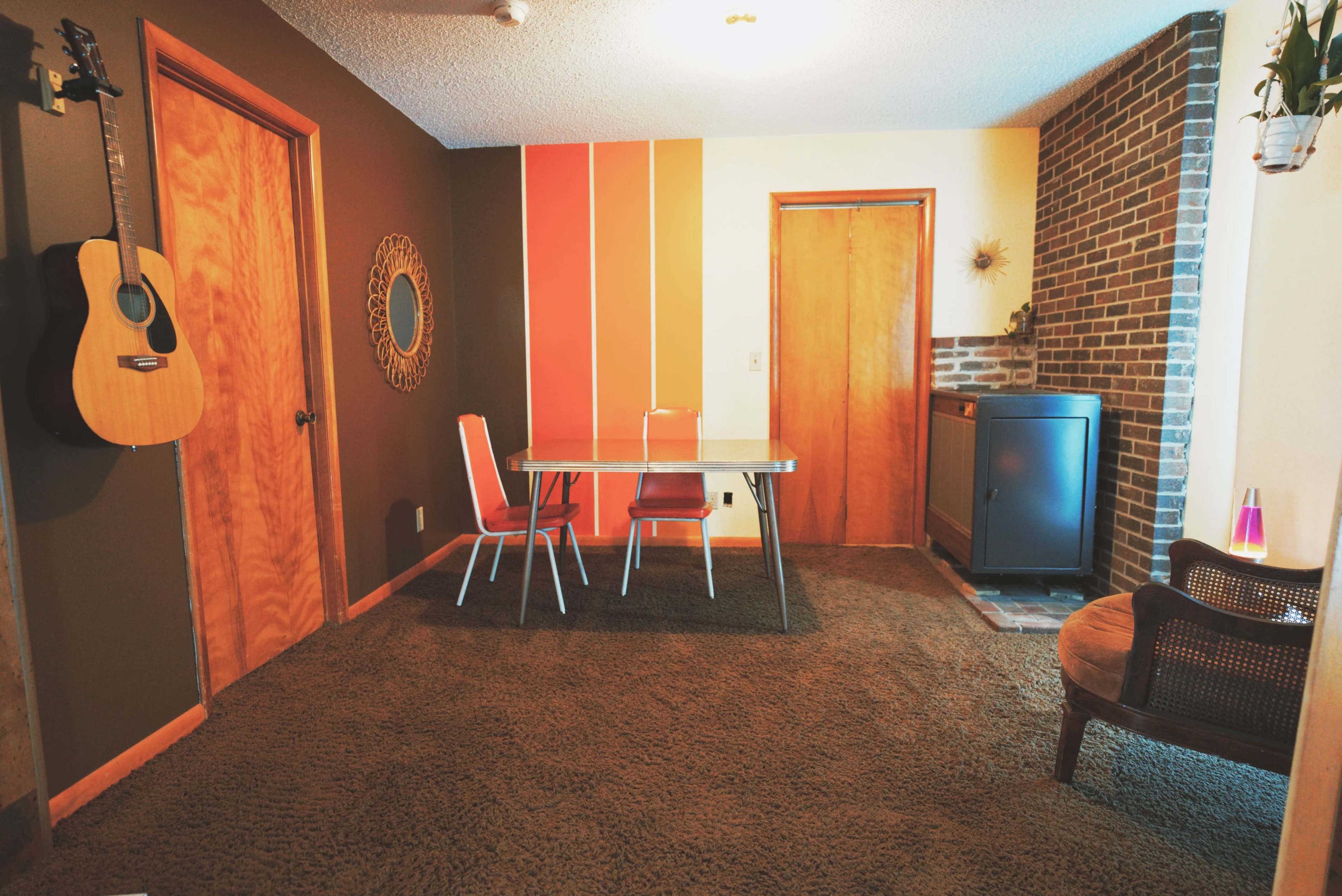 The image shows a cozy indoor room featuring a table with chairs, a wooden door, and a brick wall with a decorative panel.