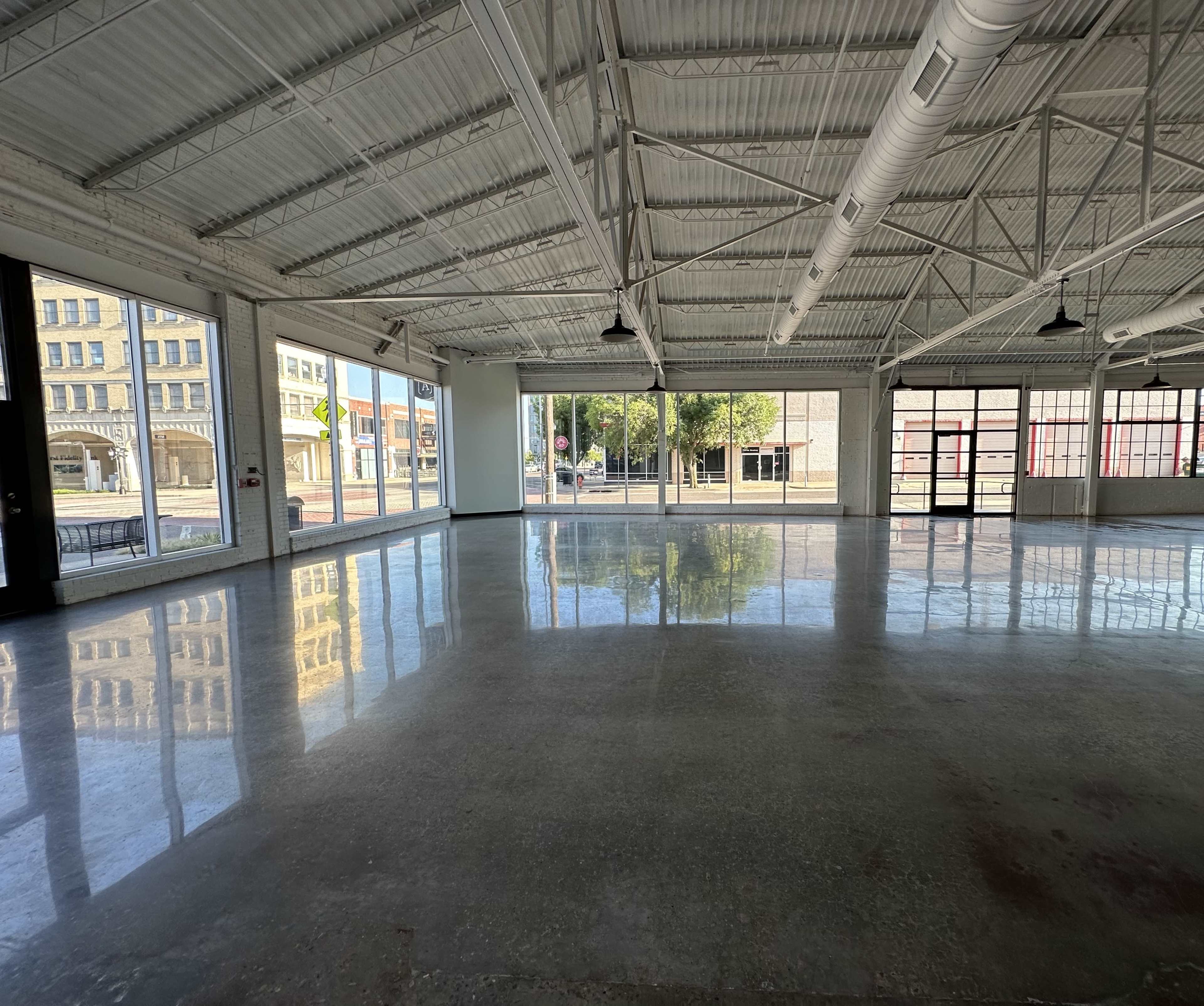 A spacious, empty room with polished concrete floors, large windows, and a high ceiling.
