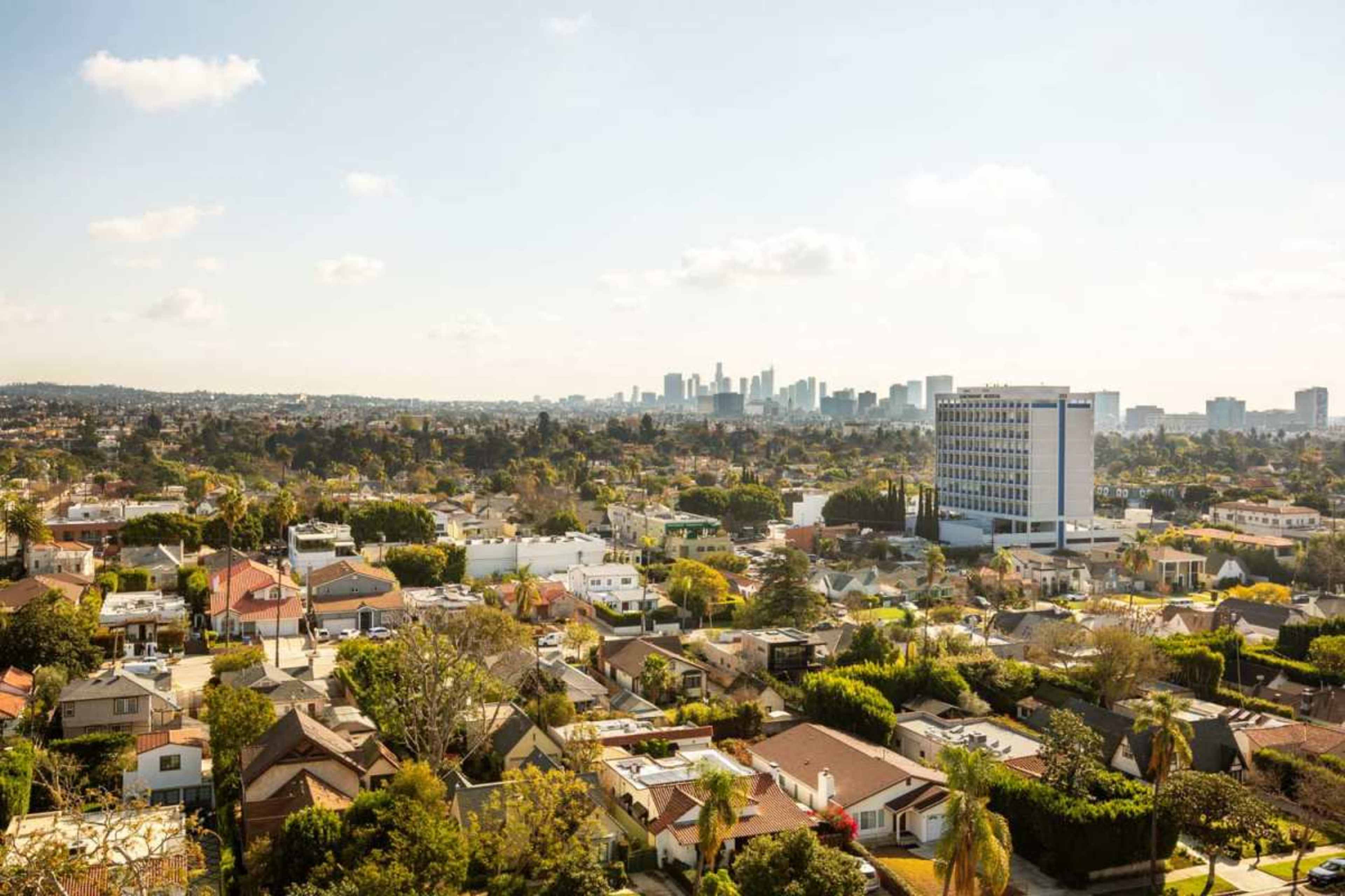 The image shows a wide view of a suburban area with residential homes and a skyline in the background.