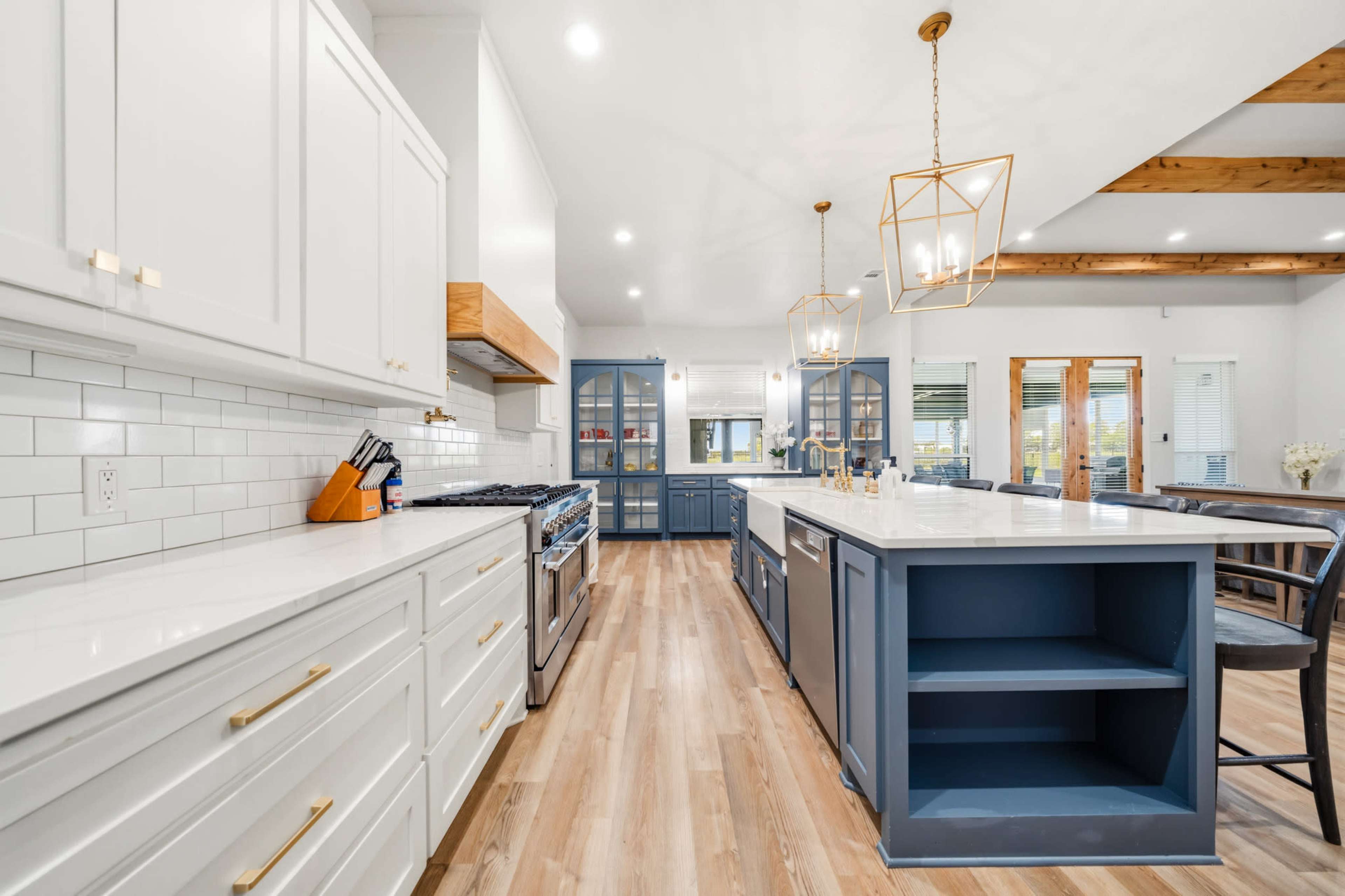 The kitchen features white cabinets, a large central island with a blue base, and a combination of modern lighting and wood accents.