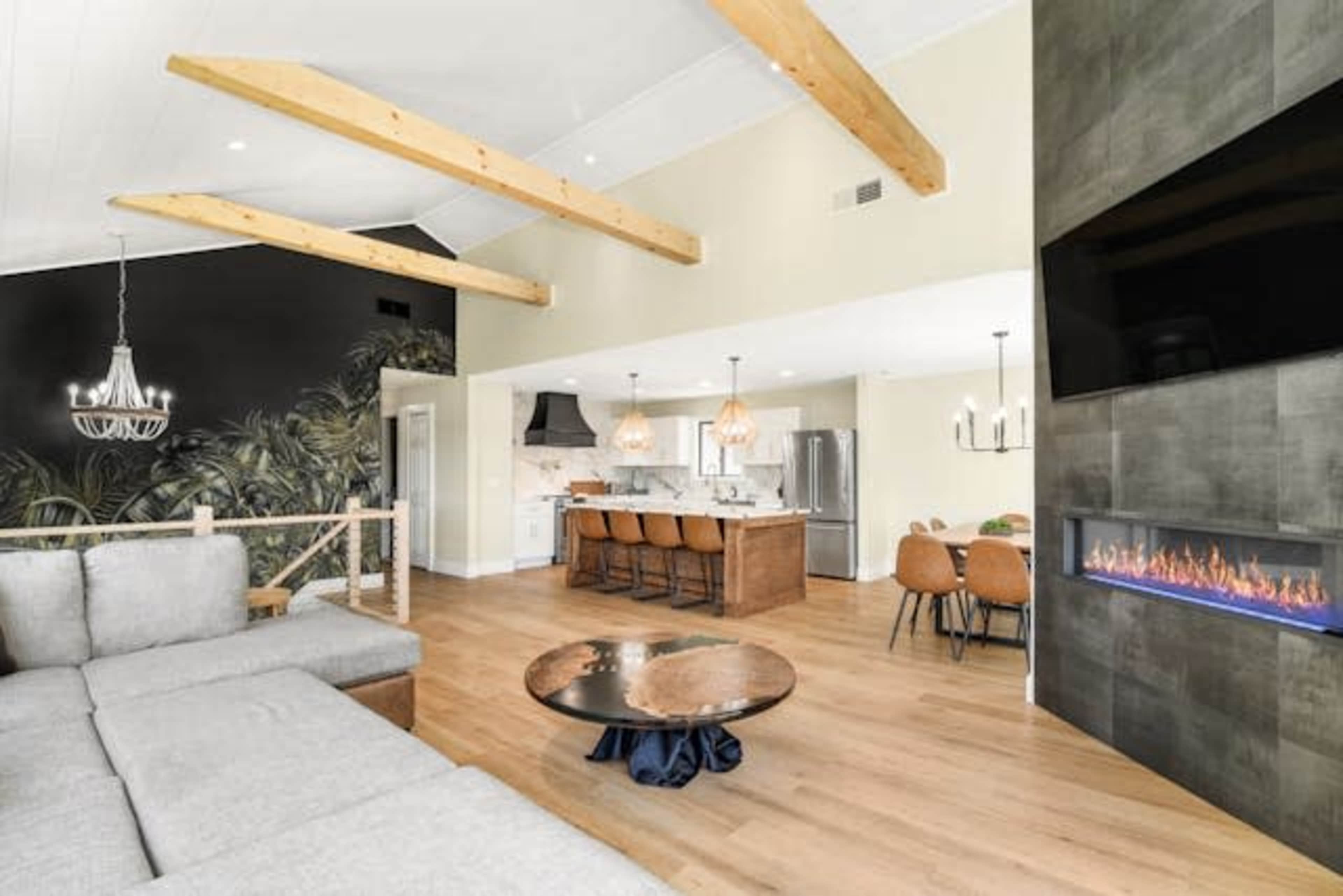 A modern living room features a sectional sofa, a round coffee table, and a kitchen in the background with pendant lights and an island.