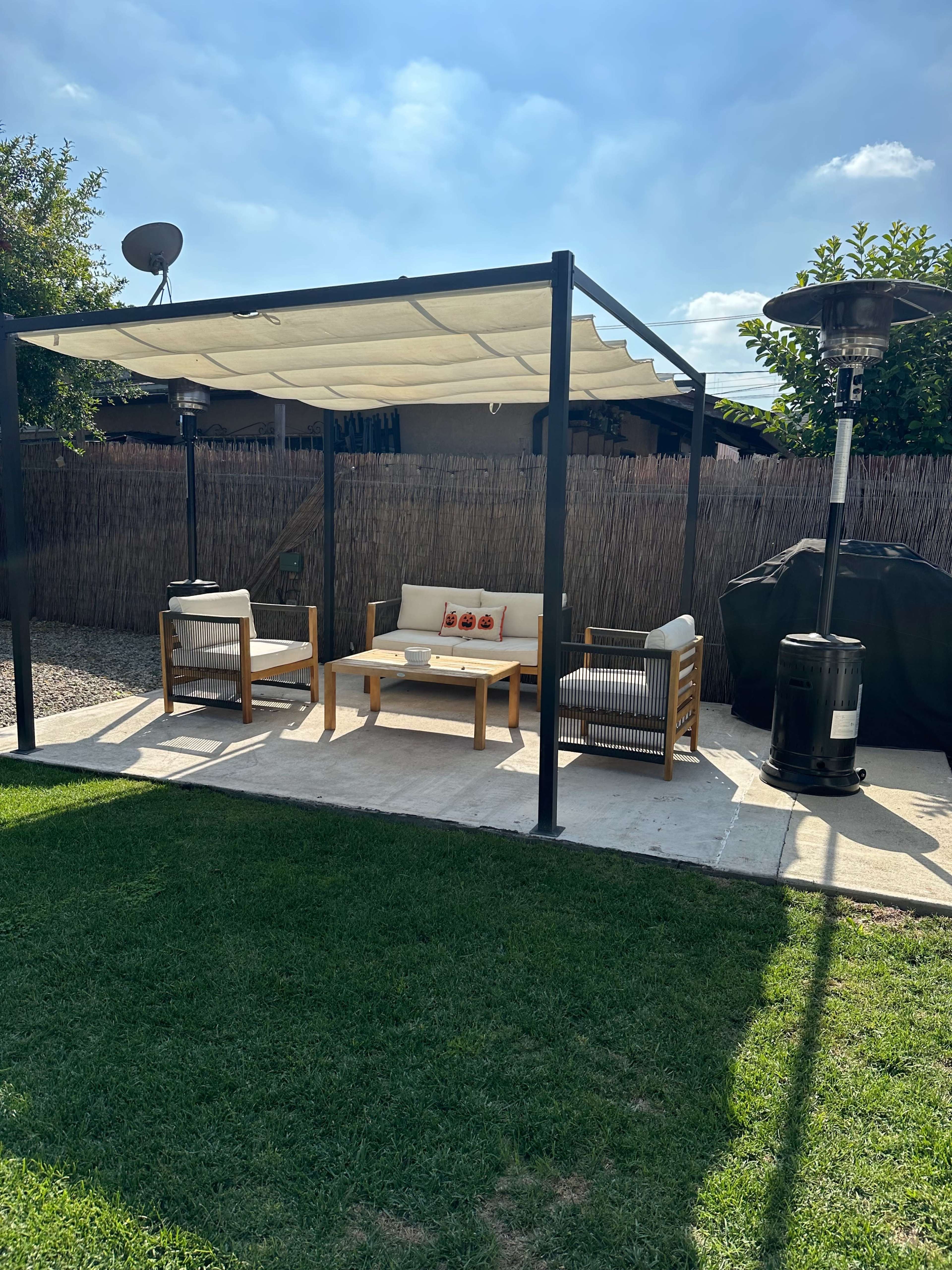 A covered outdoor seating area with a couch and chairs, accompanied by patio heaters, is situated on a grassy lawn.