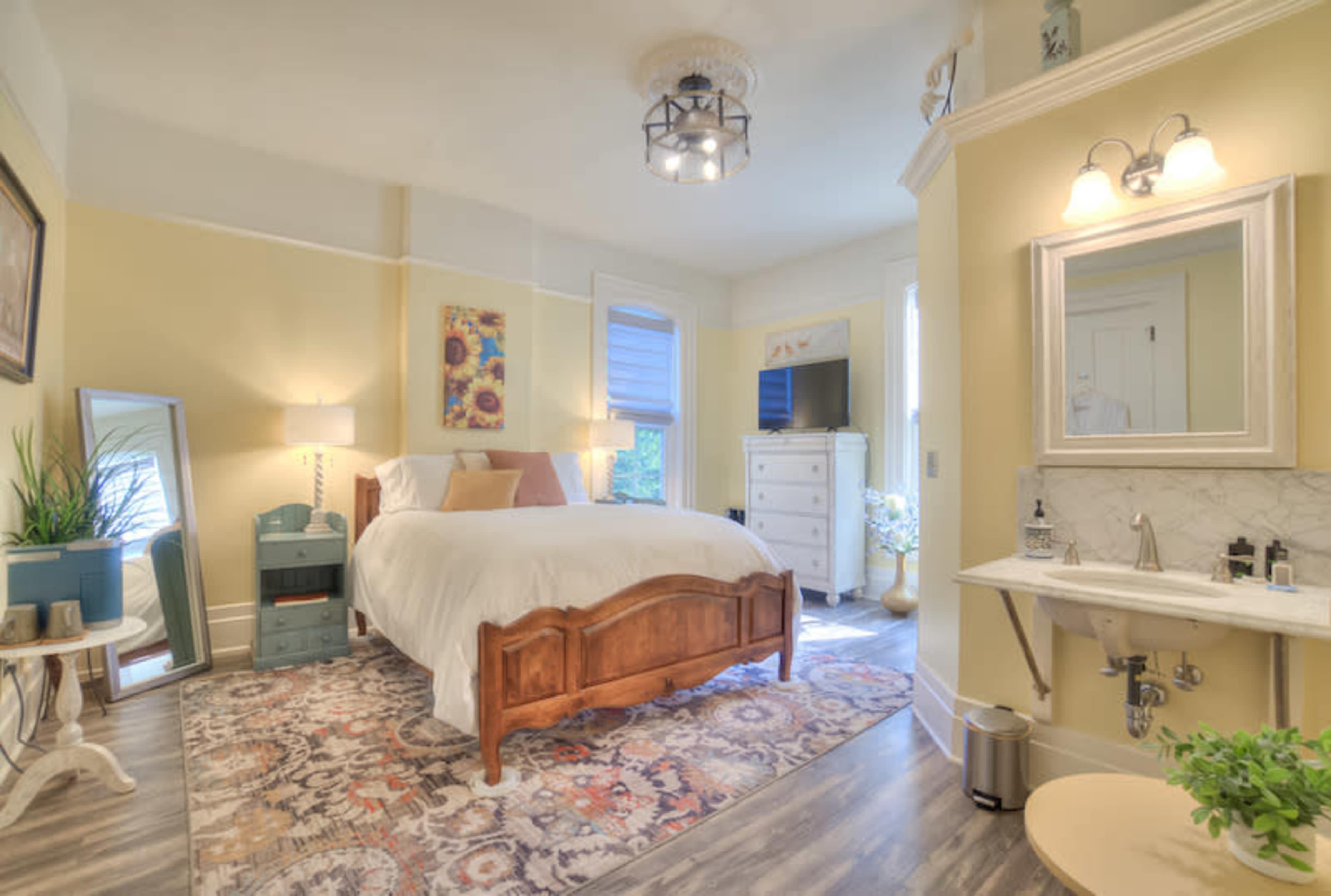 A cozy bedroom featuring a wooden bed, mirrored furniture, and a small sink area with marble accents.