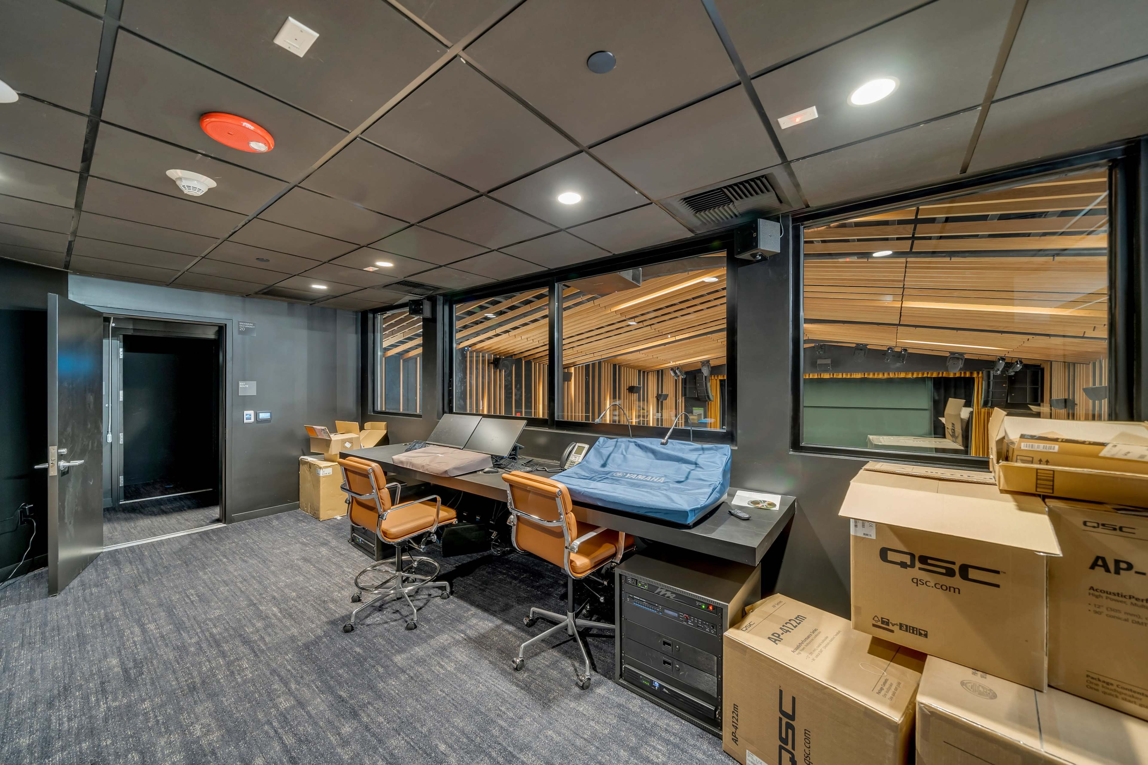 A dimly lit room with two desks equipped with computers and stacked boxes against the walls.