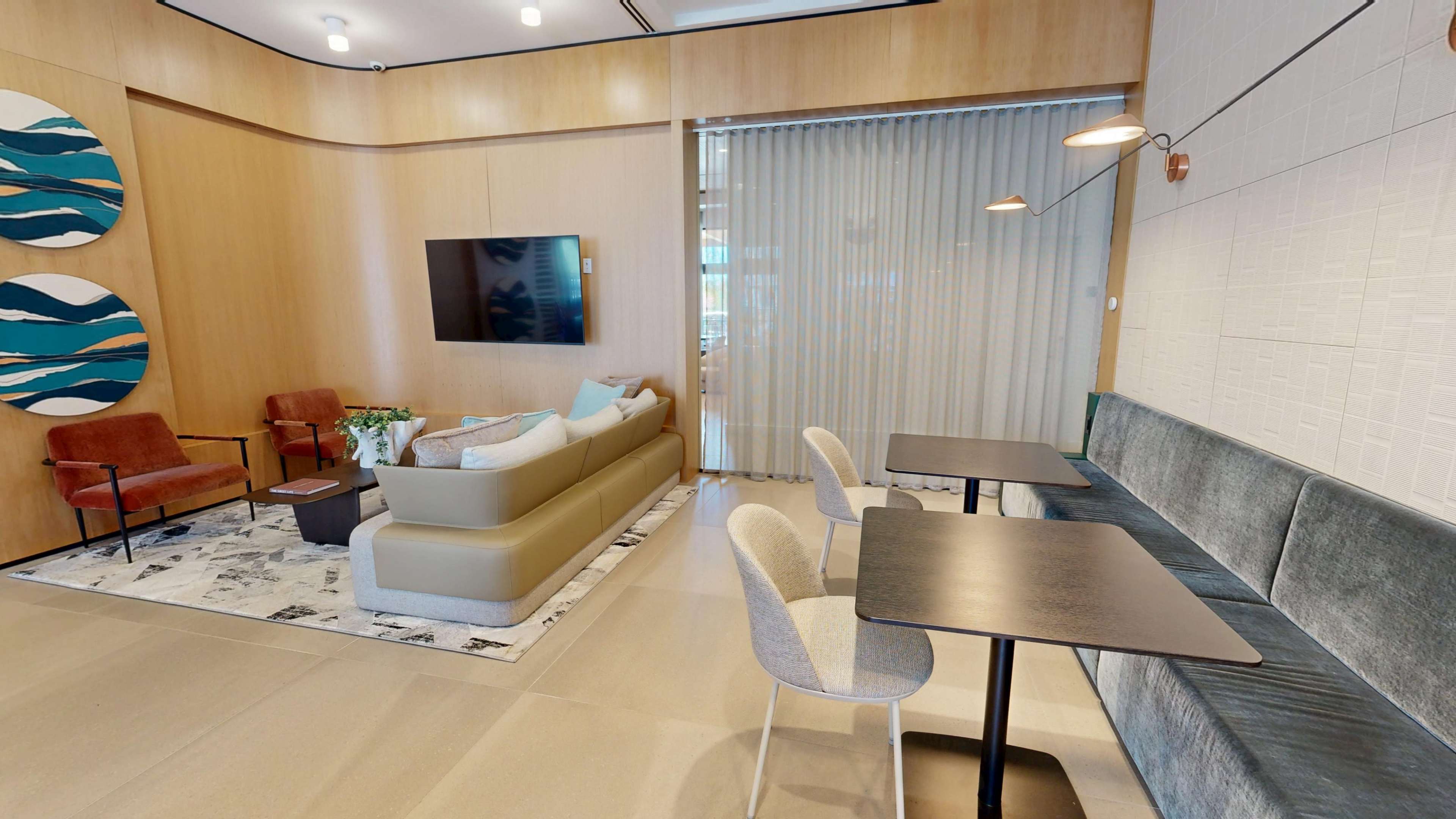 The image shows a modern interior space with a seating area featuring a sofa, armchairs, and coffee tables, alongside a dining area with tables and chairs.