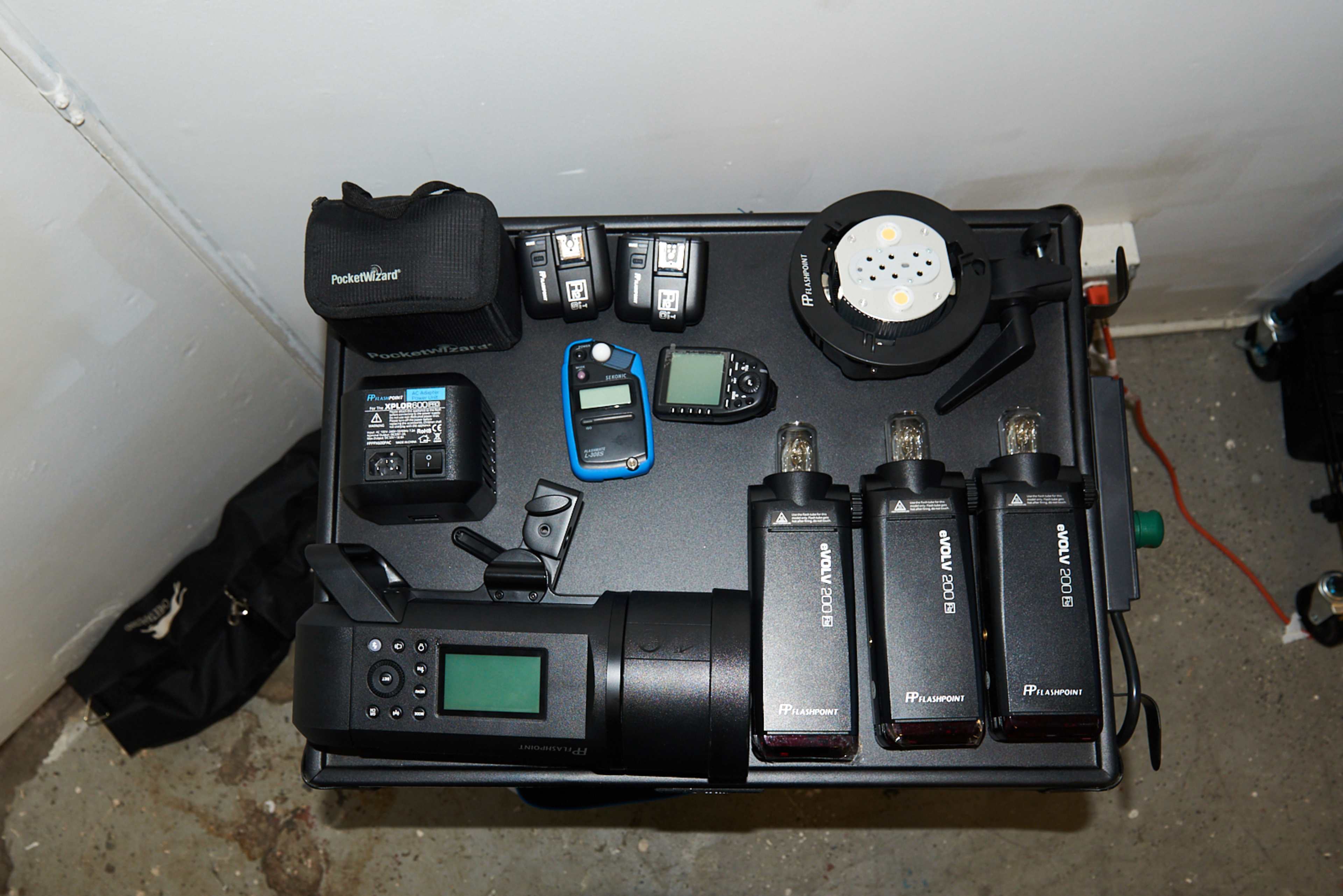 A workstation with various photography equipment, including wireless triggers, power packs, and a light meter arranged on a black table.