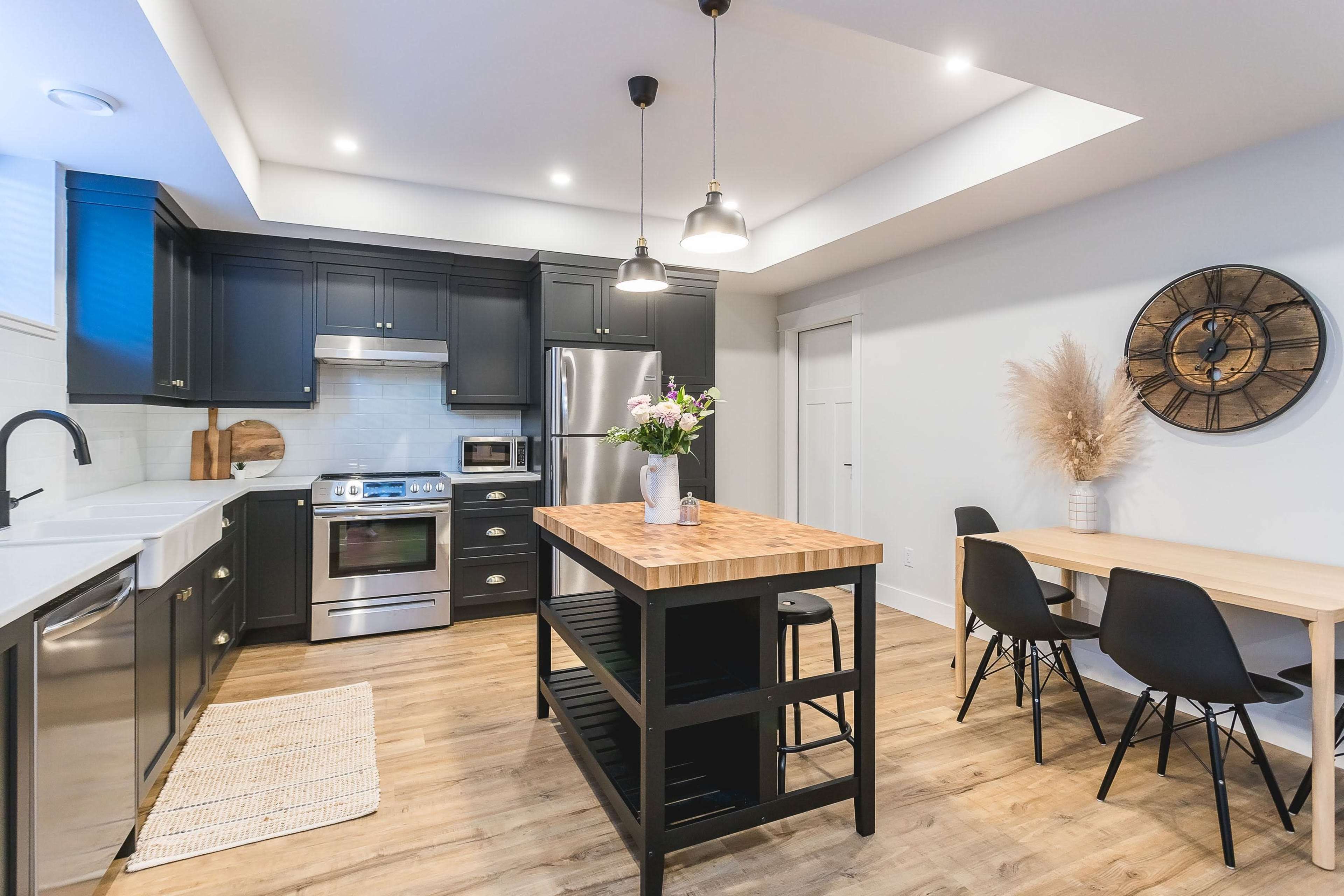 A modern kitchen with dark cabinetry, stainless steel appliances, and a central wooden island, accompanied by a dining table and decorative elements.
