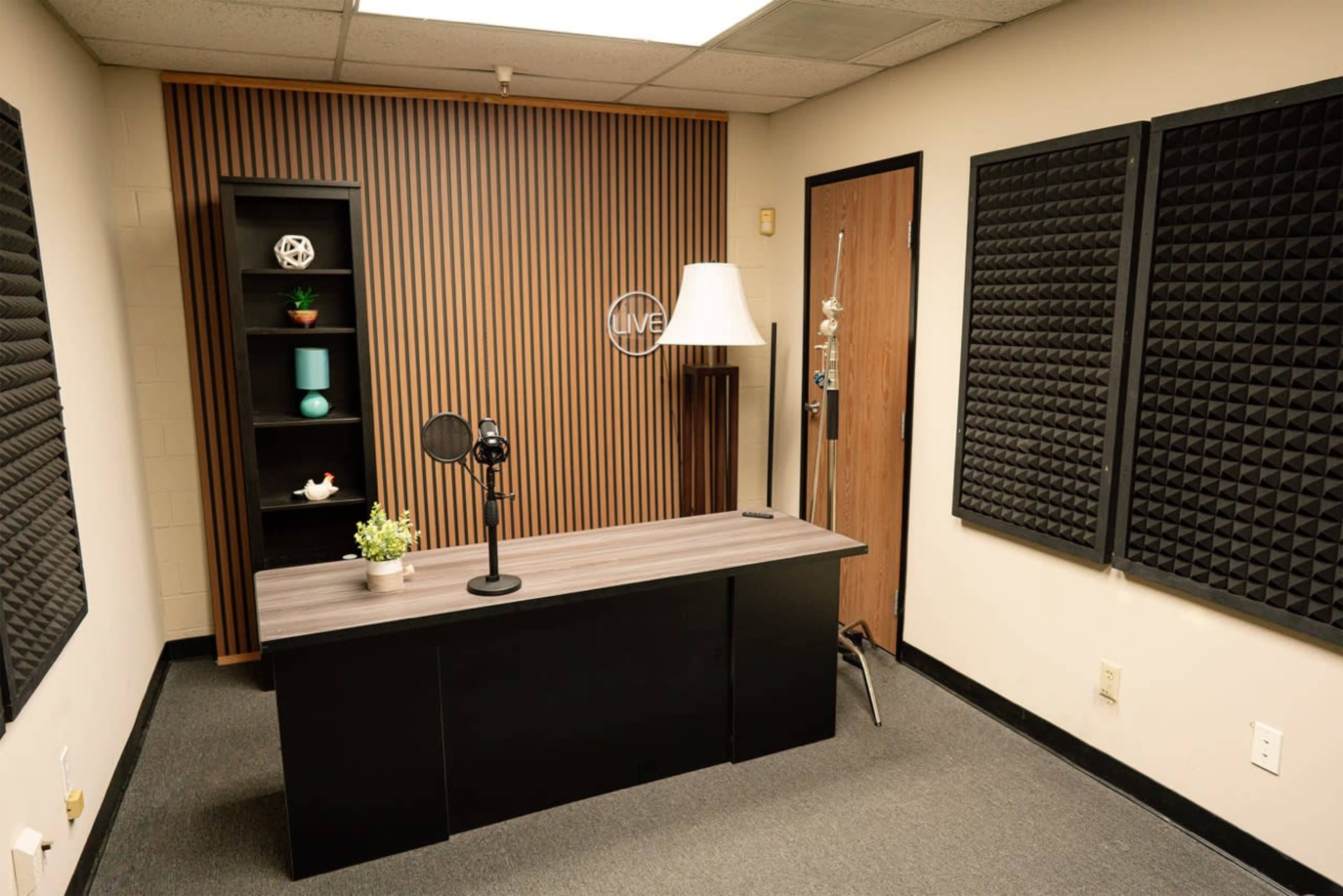 A recording studio with a table, microphone, and soundproof panels on the walls.