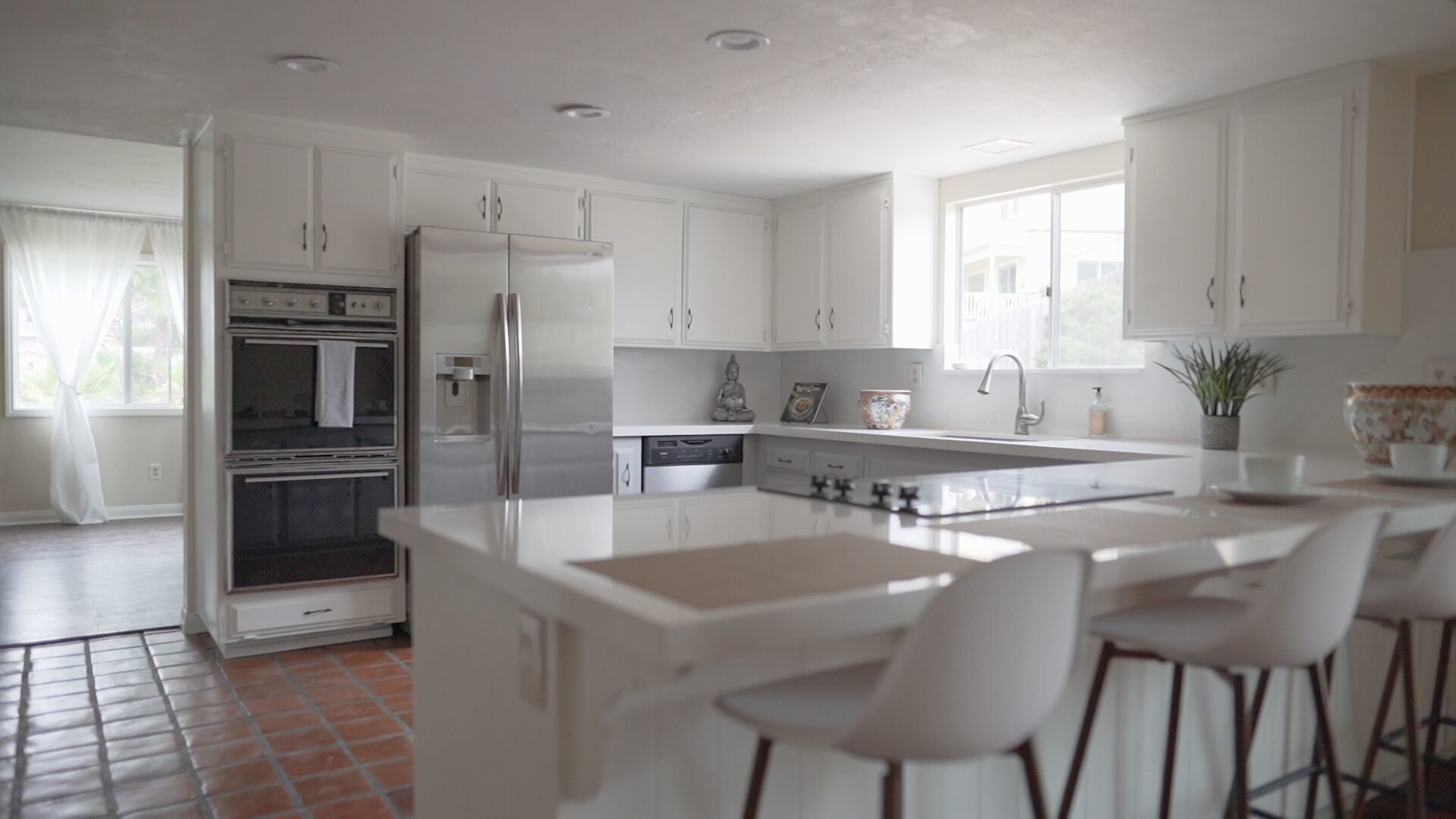 A modern kitchen with white cabinetry, stainless steel appliances, and a central island with bar stools.