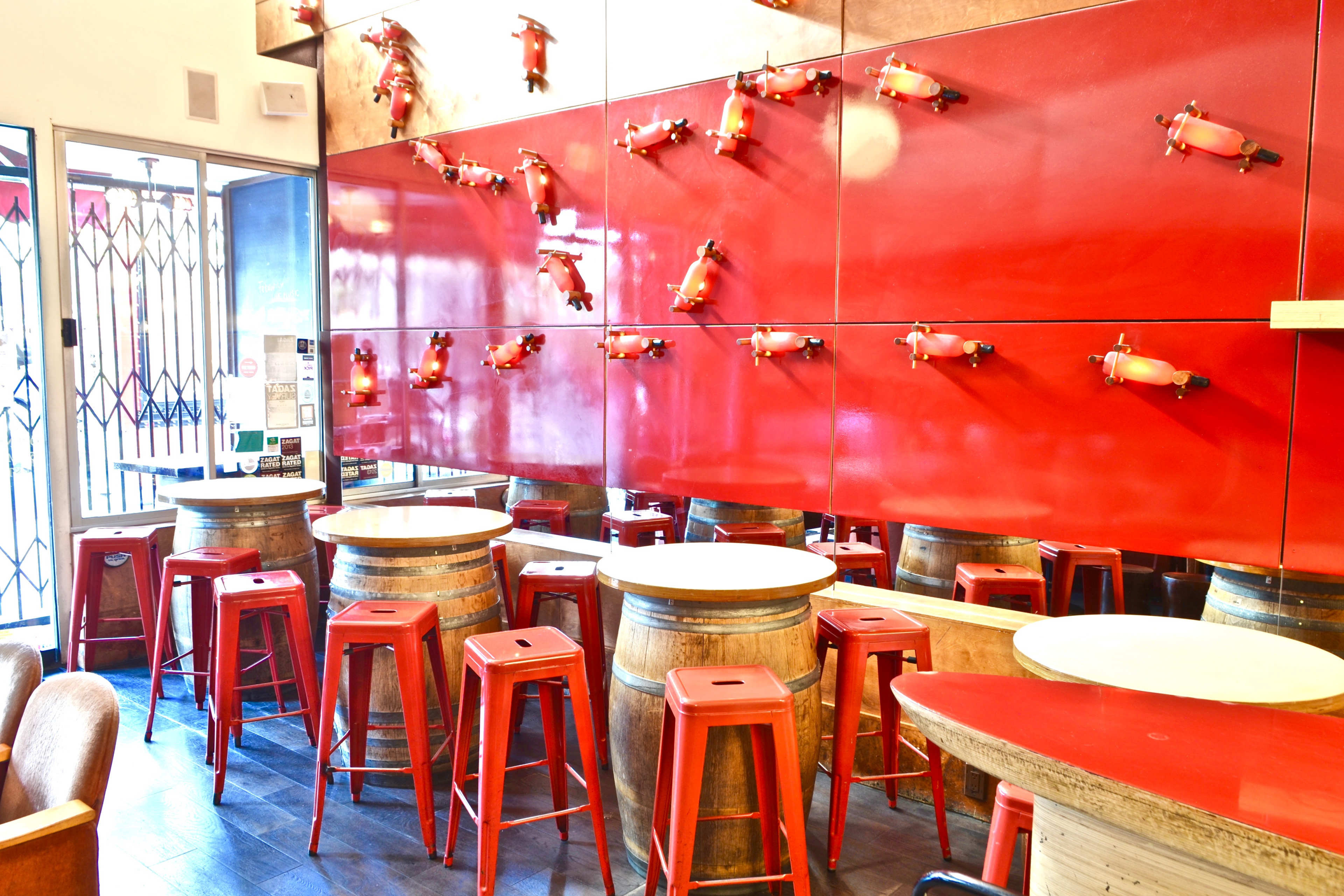 The interior features red walls with decorative elements resembling small bulls, wooden barrels as tables, and red metal stools.