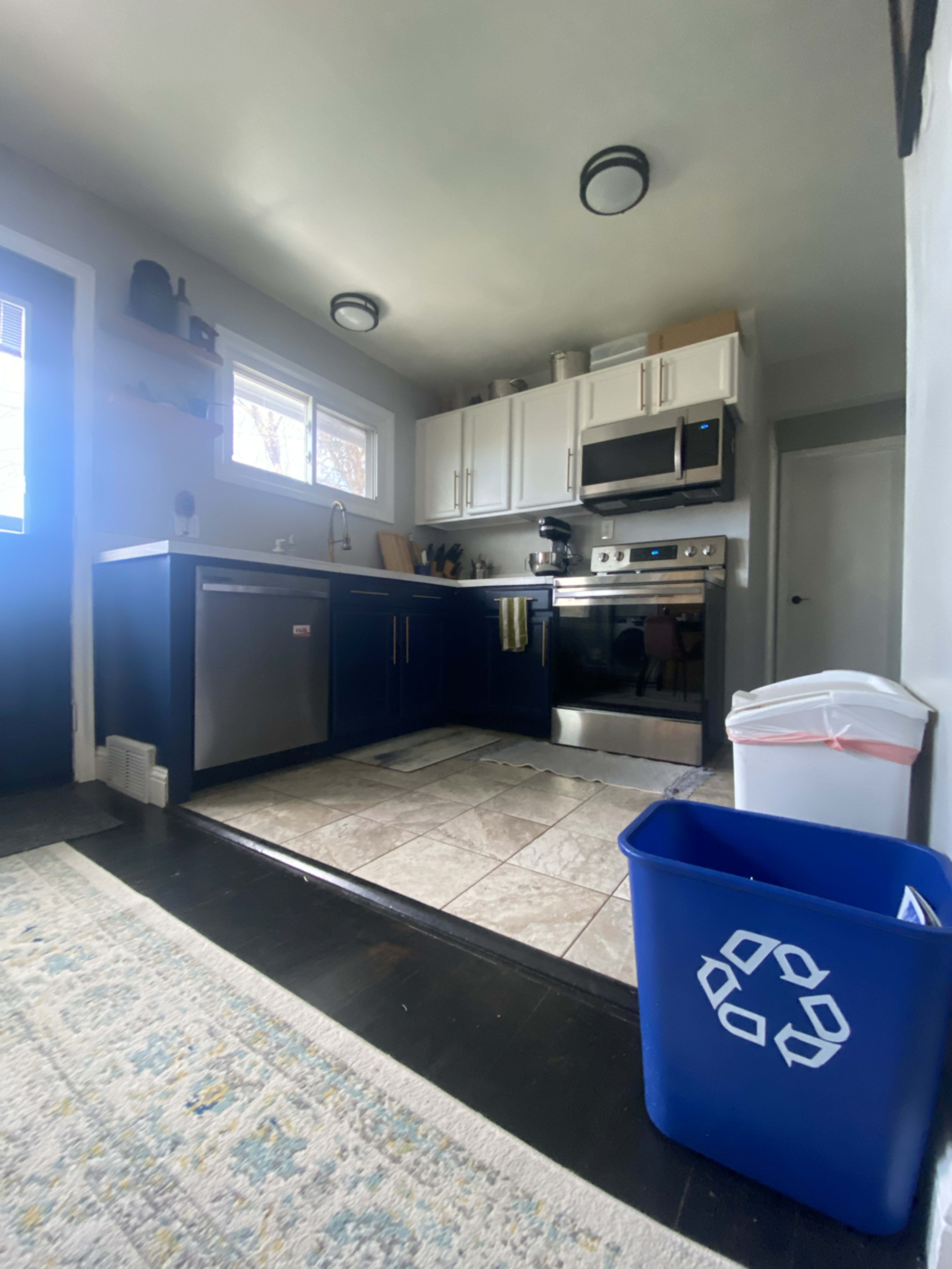 A kitchen featuring dark blue cabinets, stainless steel appliances, a tile floor, and a recycling bin in the corner.