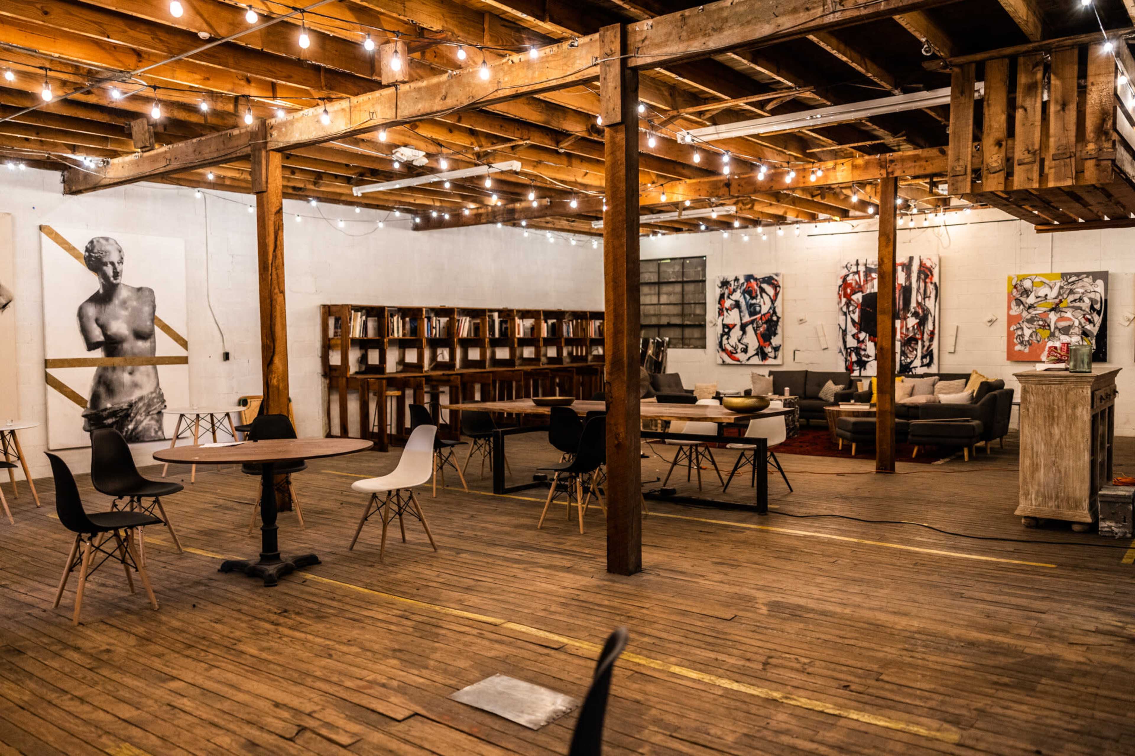 An industrial-style open space with wooden floors, exposed beams, and various seating arrangements surrounded by artwork on the walls.