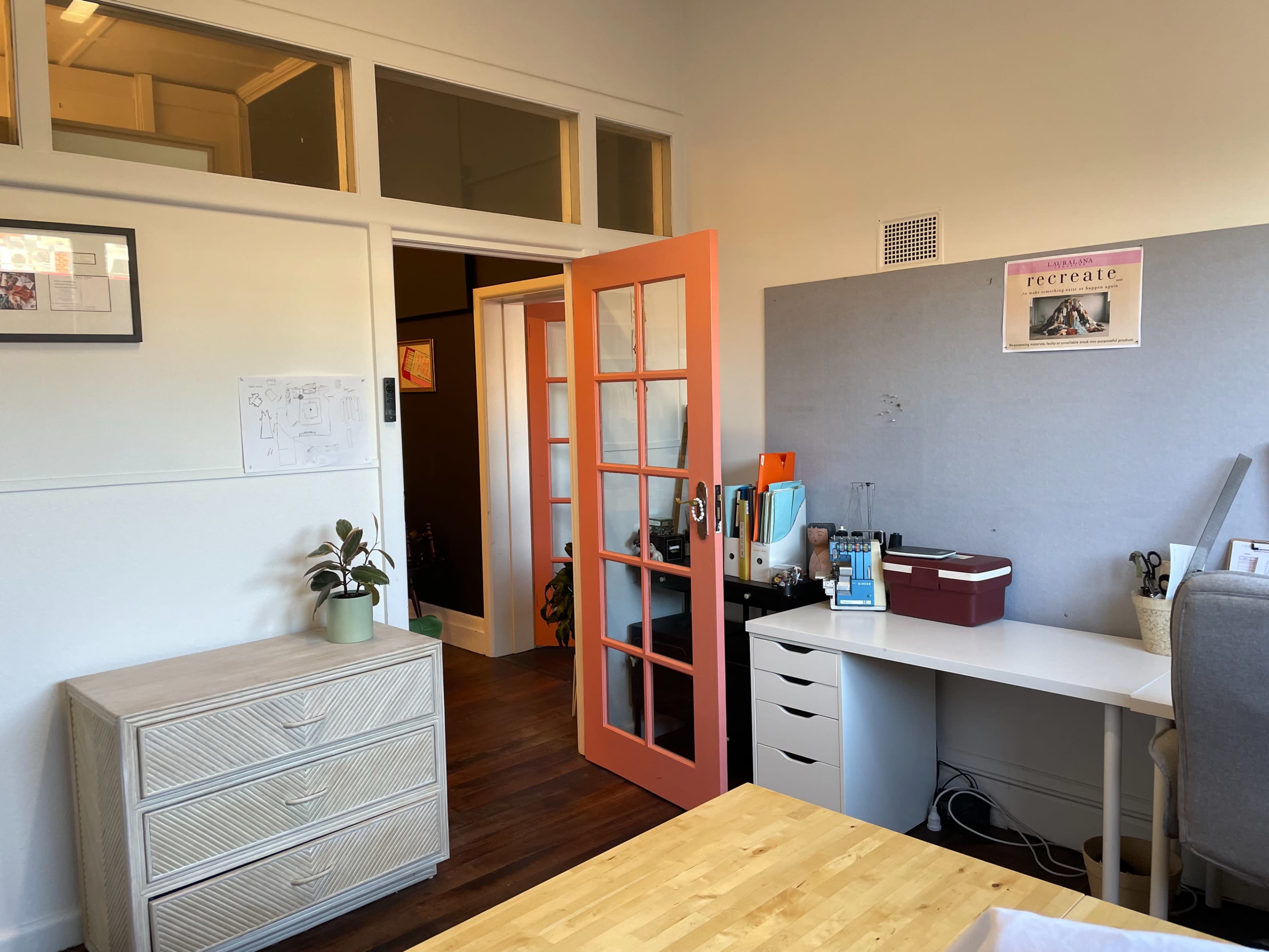 The image shows a room with a desk, a dresser, a partially open pink door, and a bulletin board on the wall.