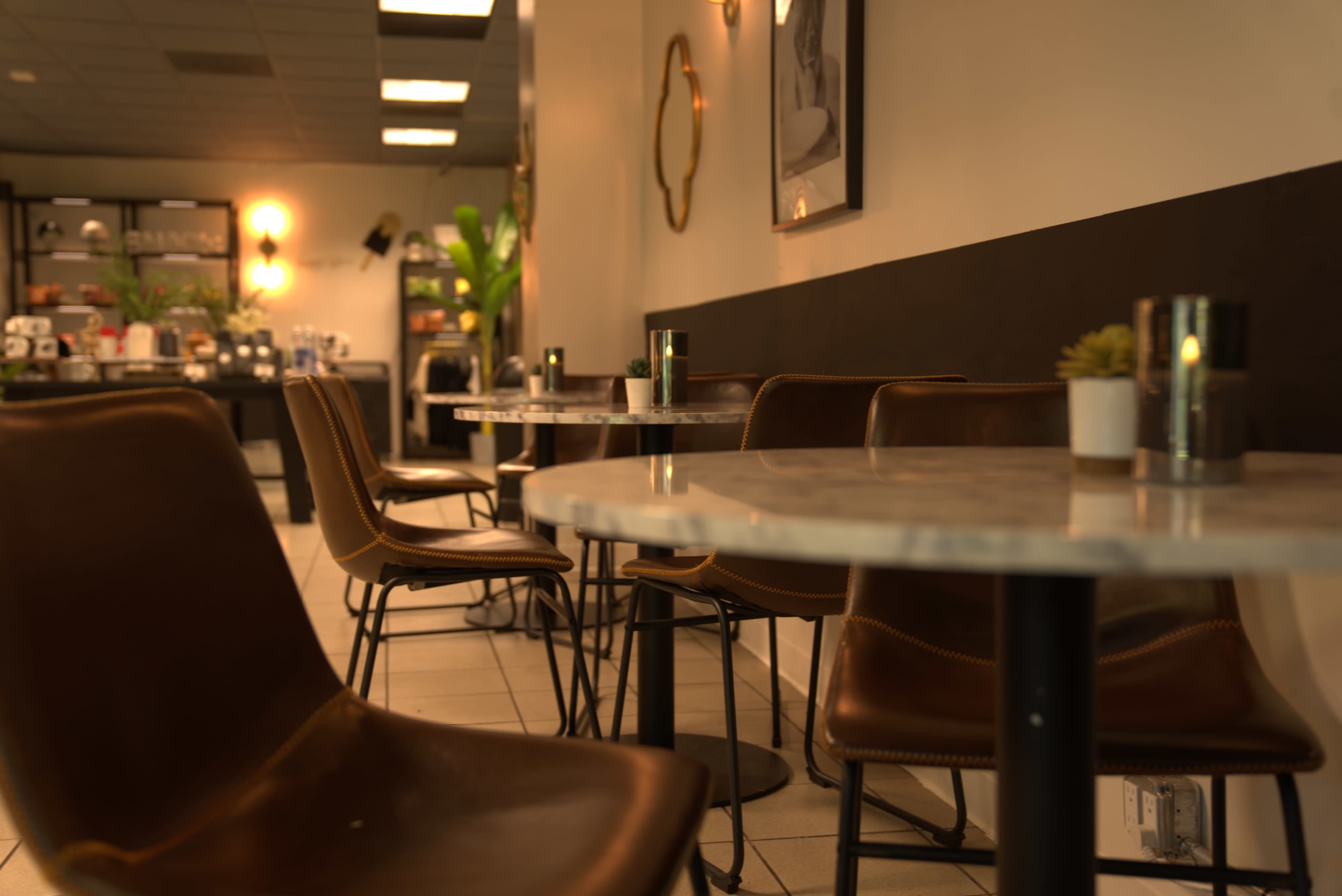 A modern café interior with several round marble-top tables surrounded by brown leather chairs.