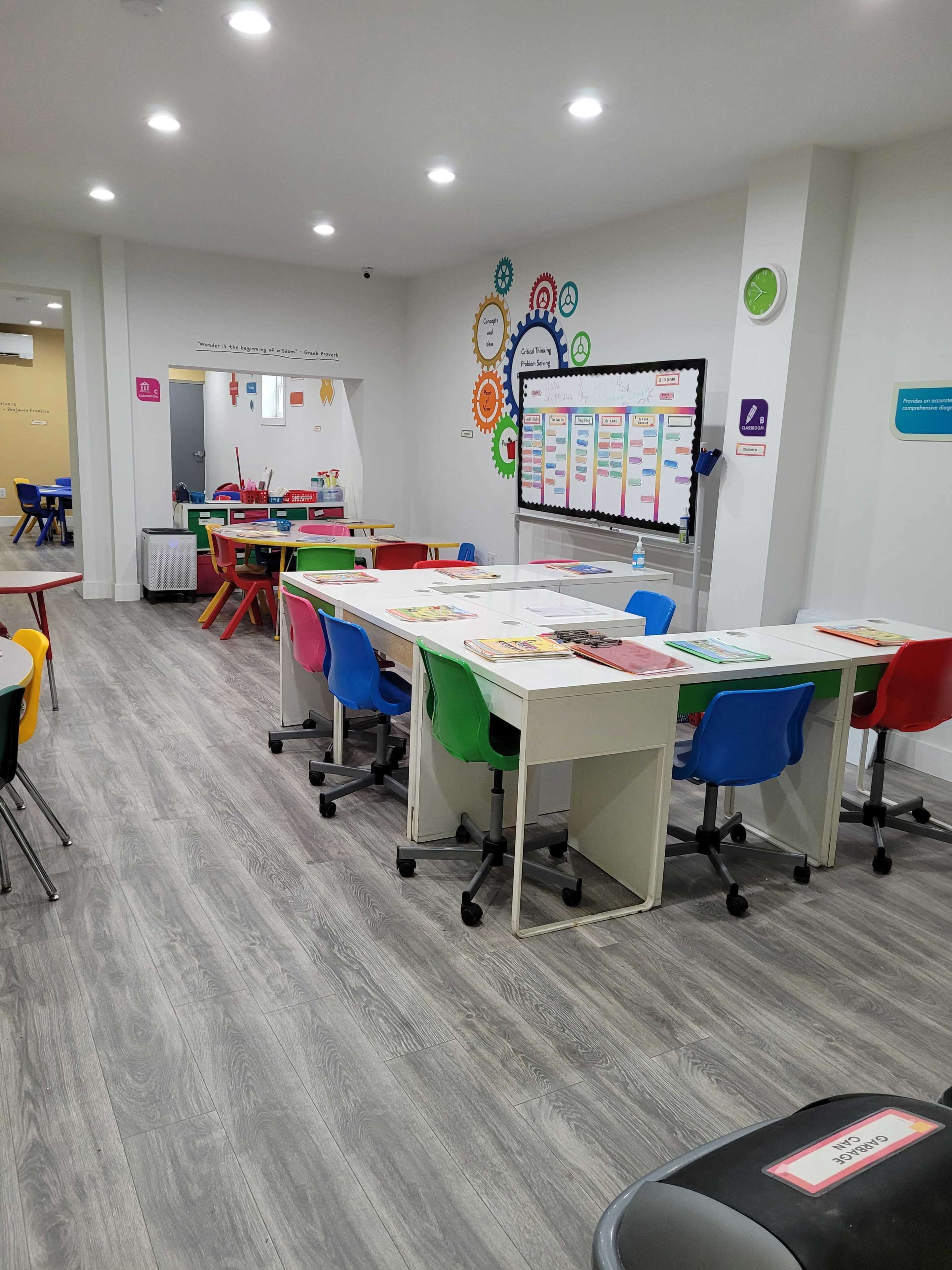 A well-organized classroom with colorful chairs, tables, and a bulletin board displaying educational materials.