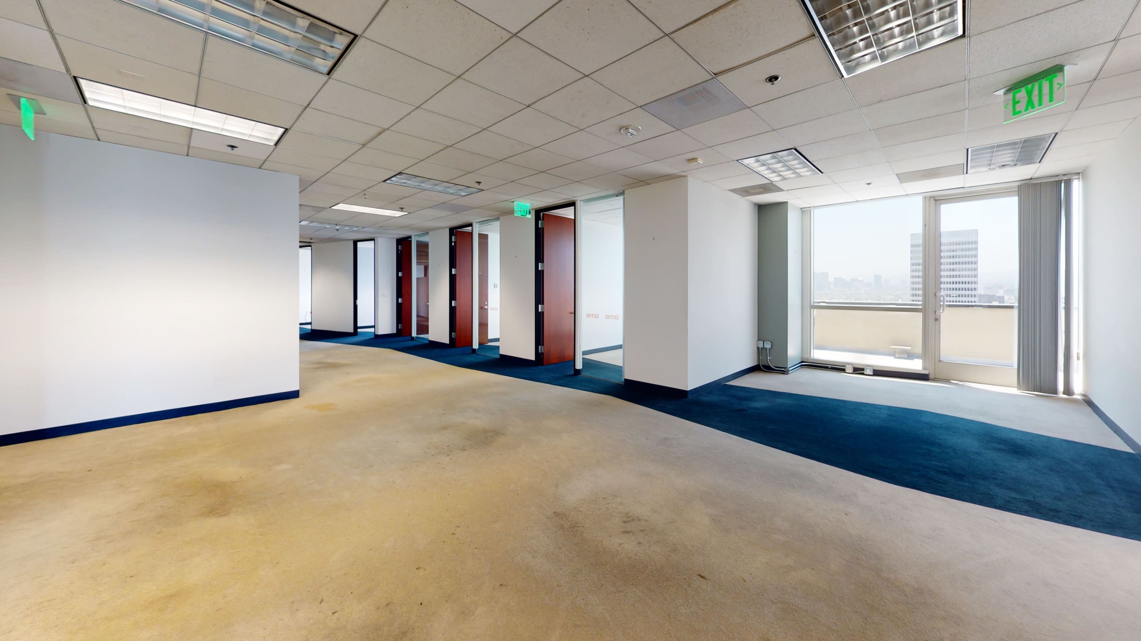 The image shows an empty office space with blue carpeting and glass-walled offices along one side.