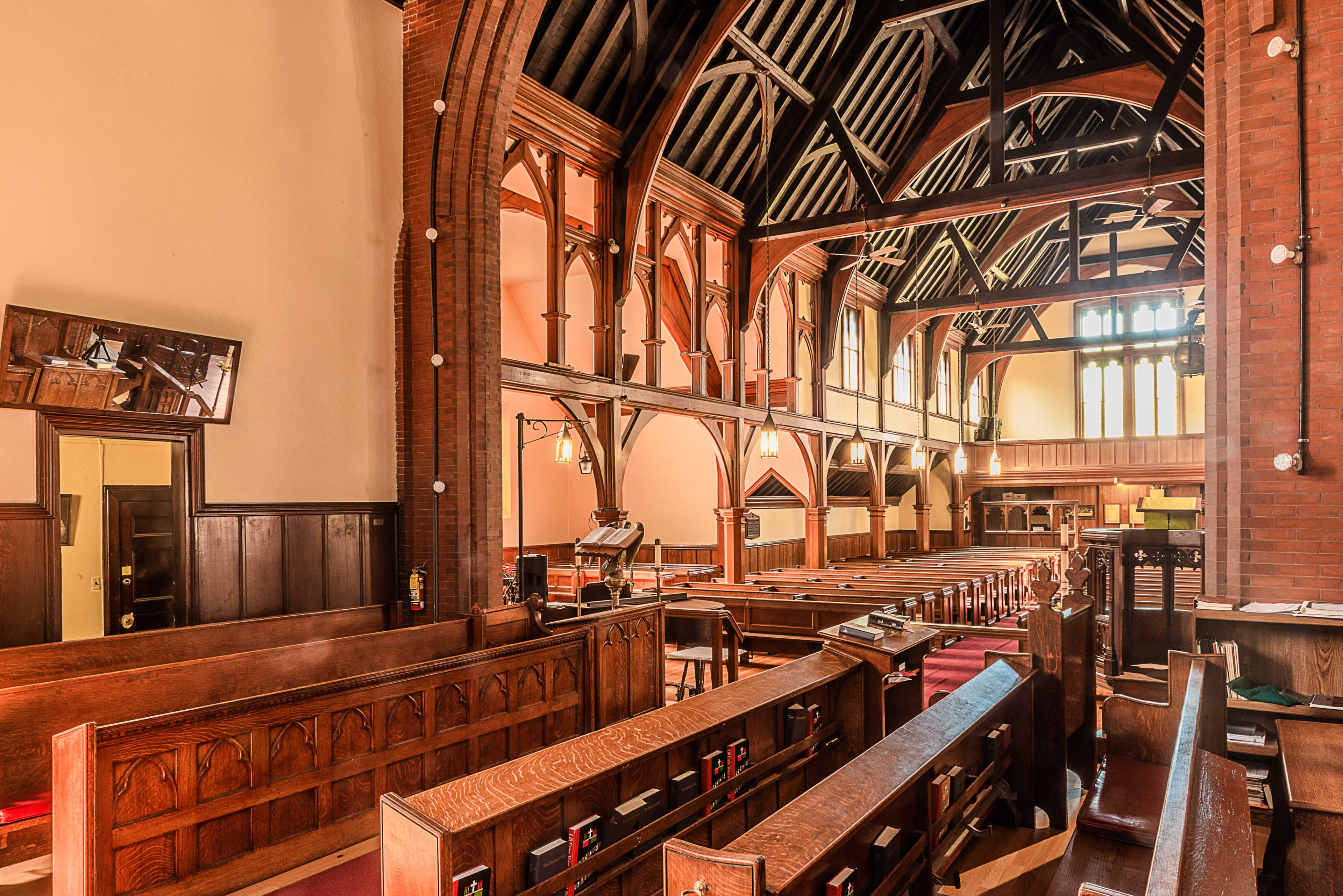 The interior of a church features wooden pews, a high wooden-beamed ceiling, and large windows that allow light to fill the space.