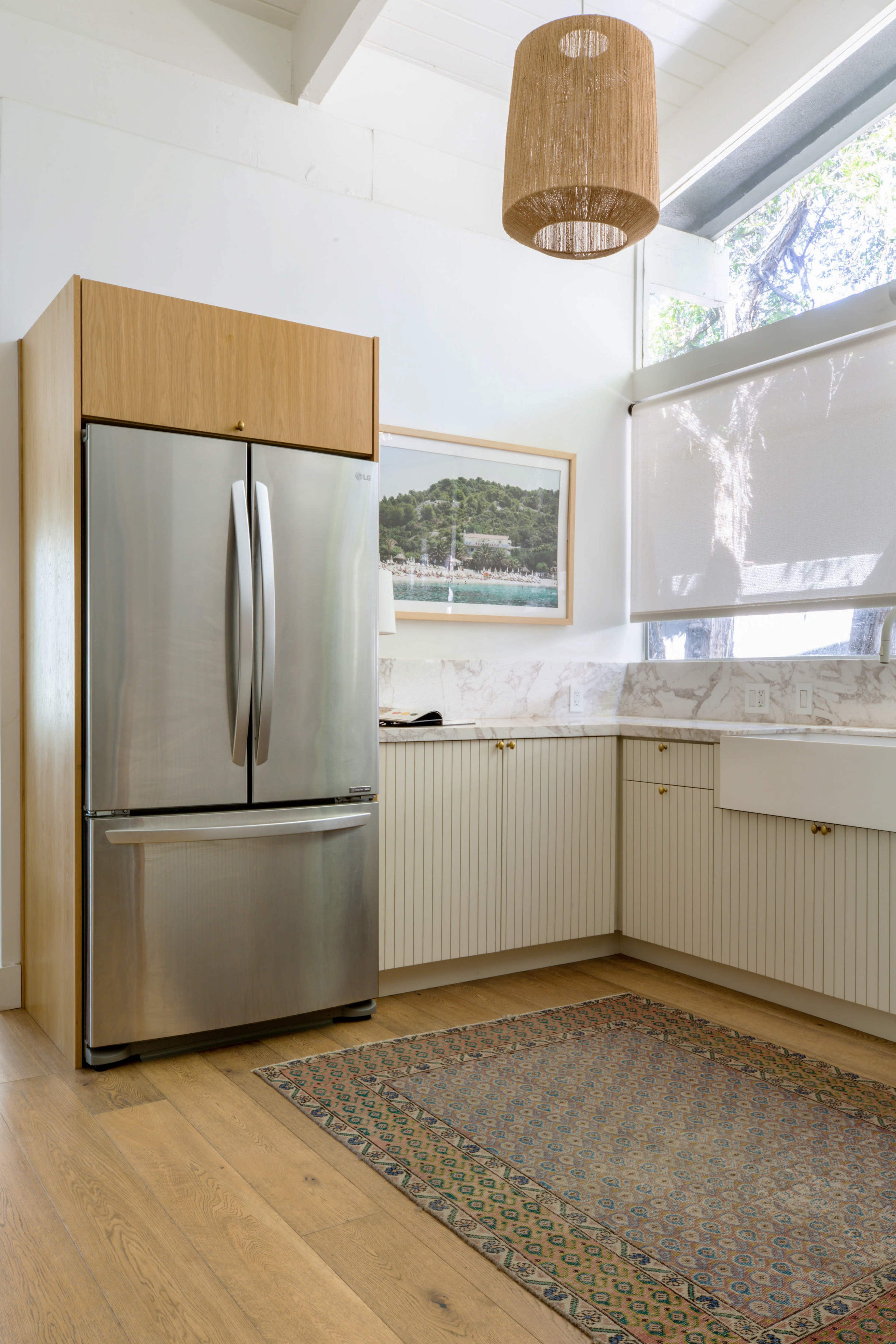 The image features a stainless steel refrigerator placed next to a light-colored kitchen counter with decorative wood paneling and a rug on the wooden floor.