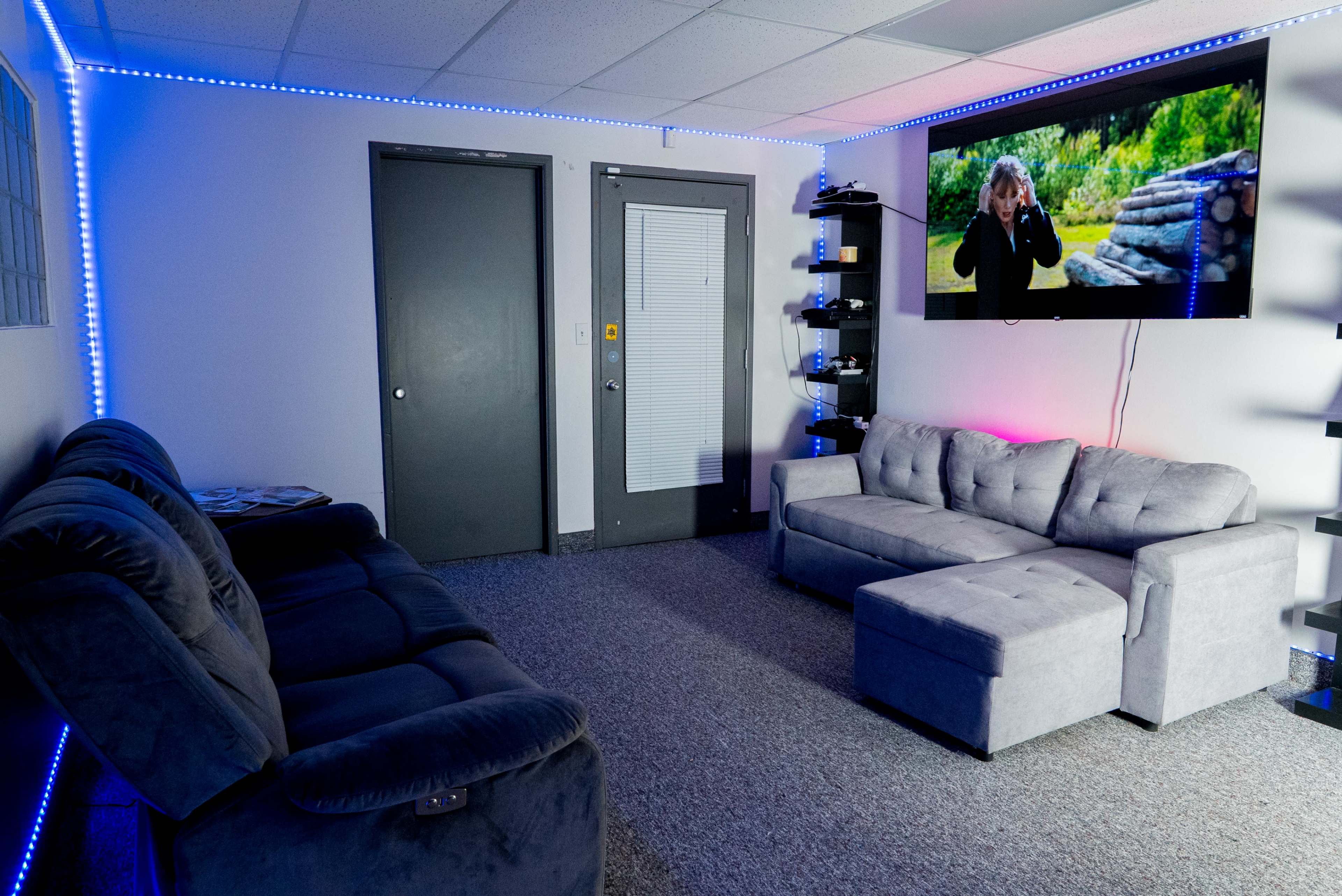 The room features two sofas, a television mounted on the wall displaying a scene, and LED lights around the perimeter.