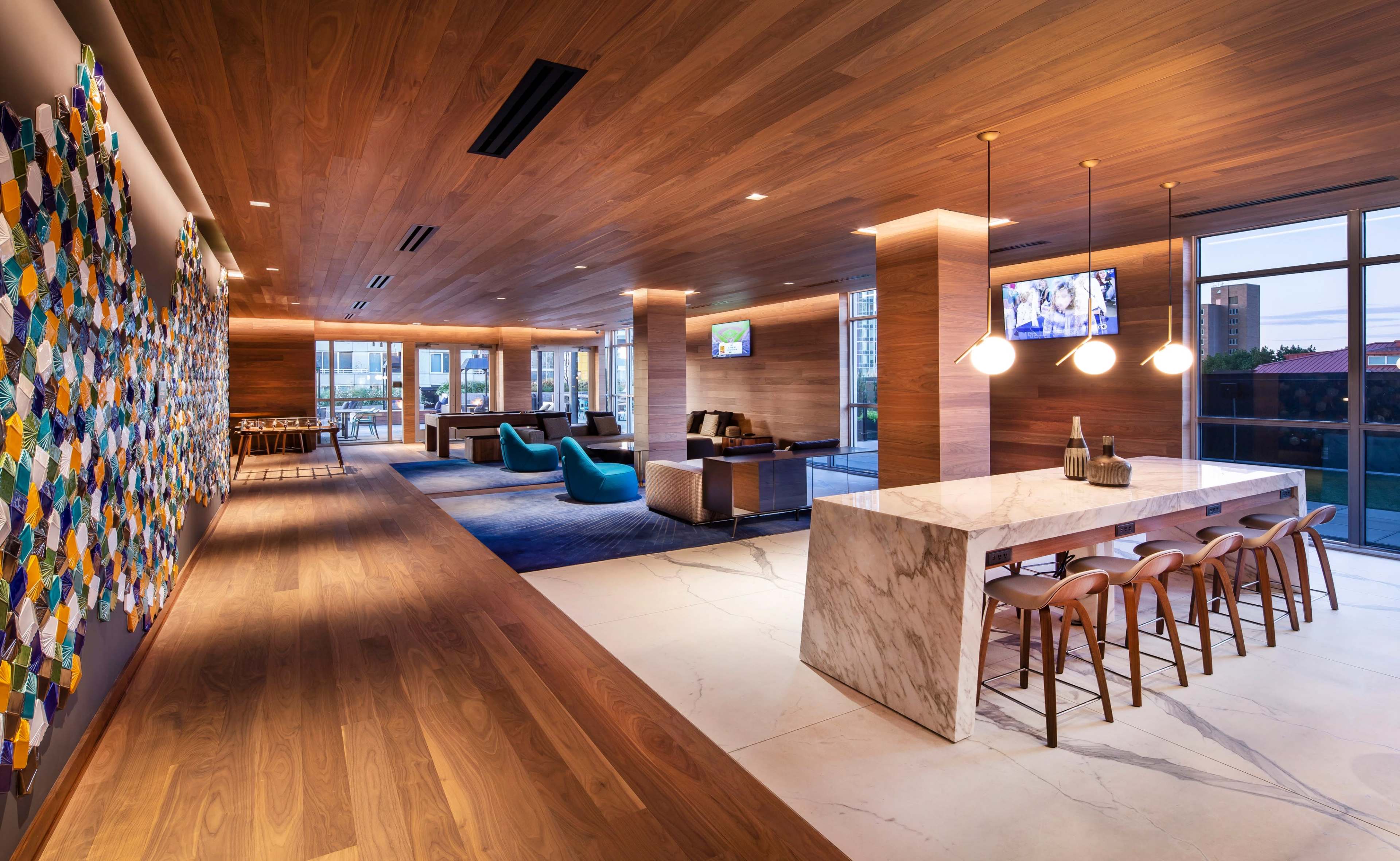 A modern lounge area with wooden walls, a marble bar, and various seating arrangements, including a wall adorned with colorful paper squares.