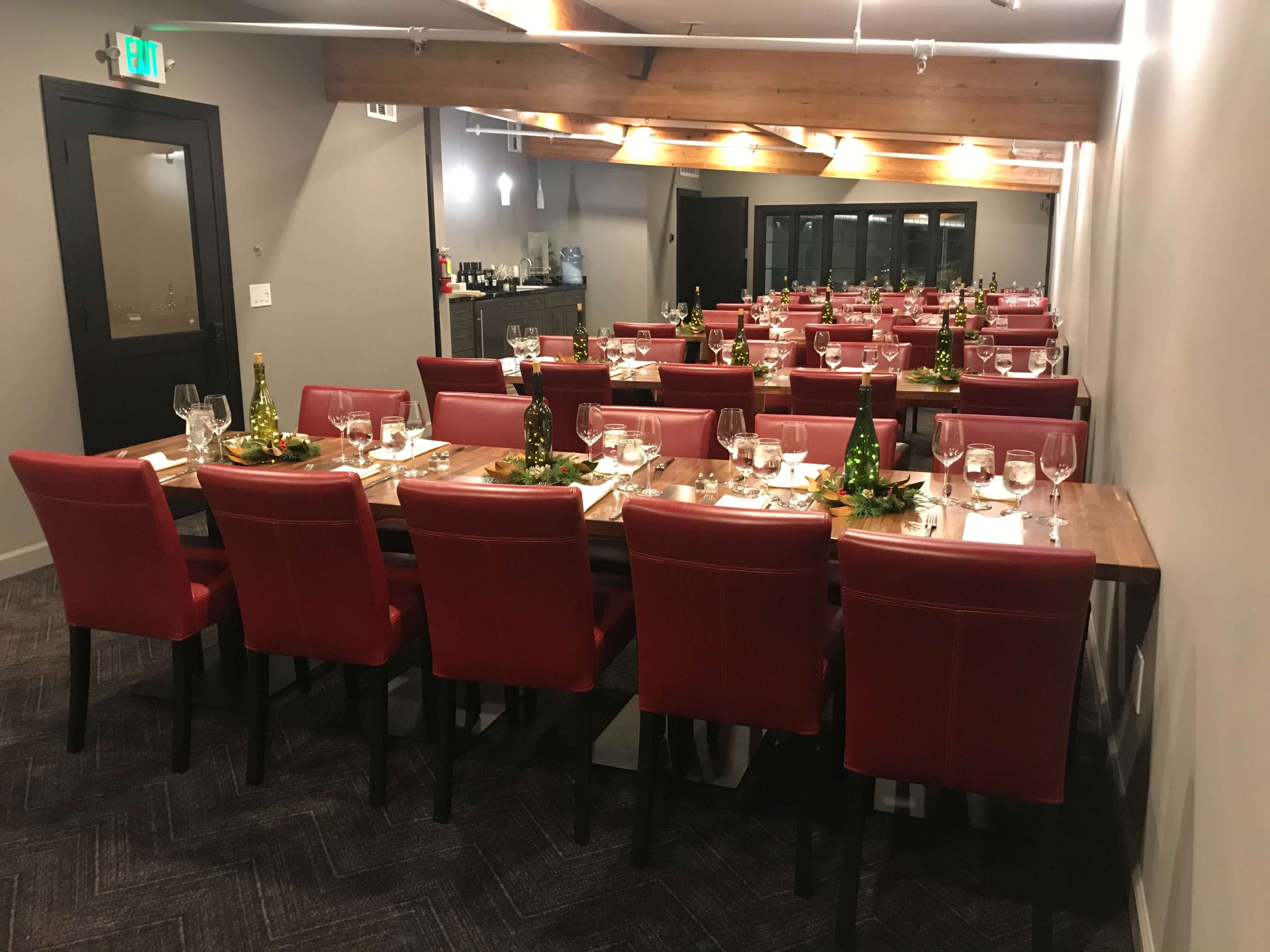 A spacious dining room is set with long wooden tables arranged for a formal meal, featuring red chairs and elegant table settings.