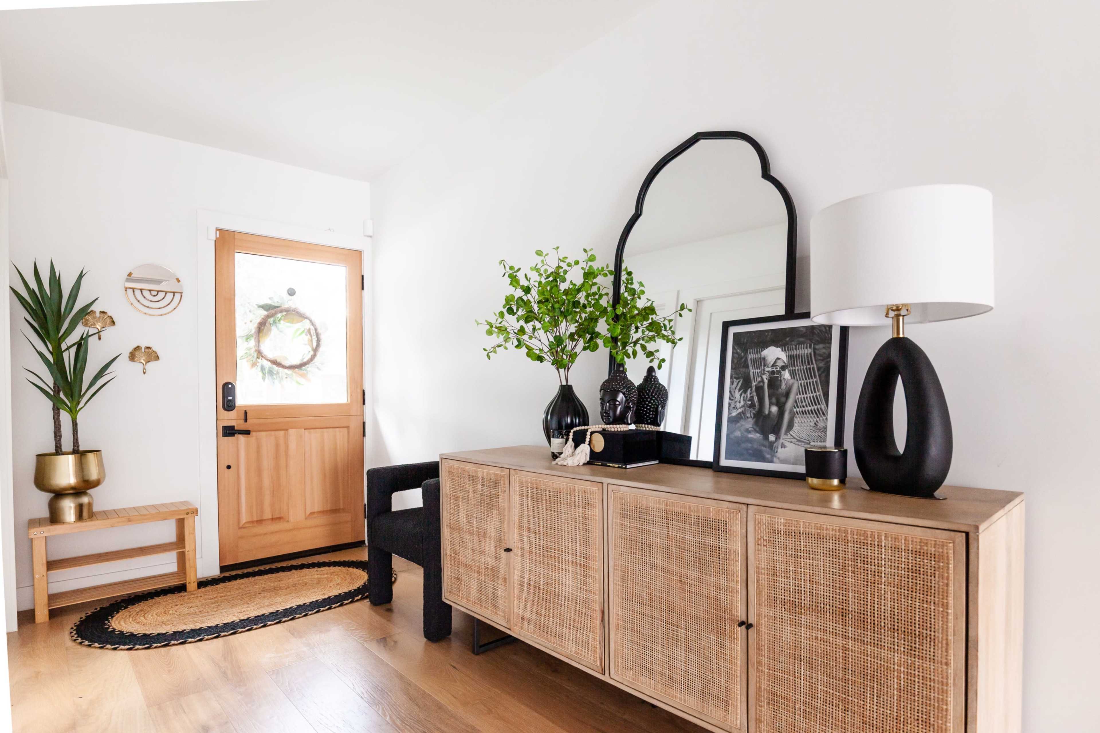 A well-lit entryway features a wooden door, a console table with decorative items, a floor lamp, and a potted plant.
