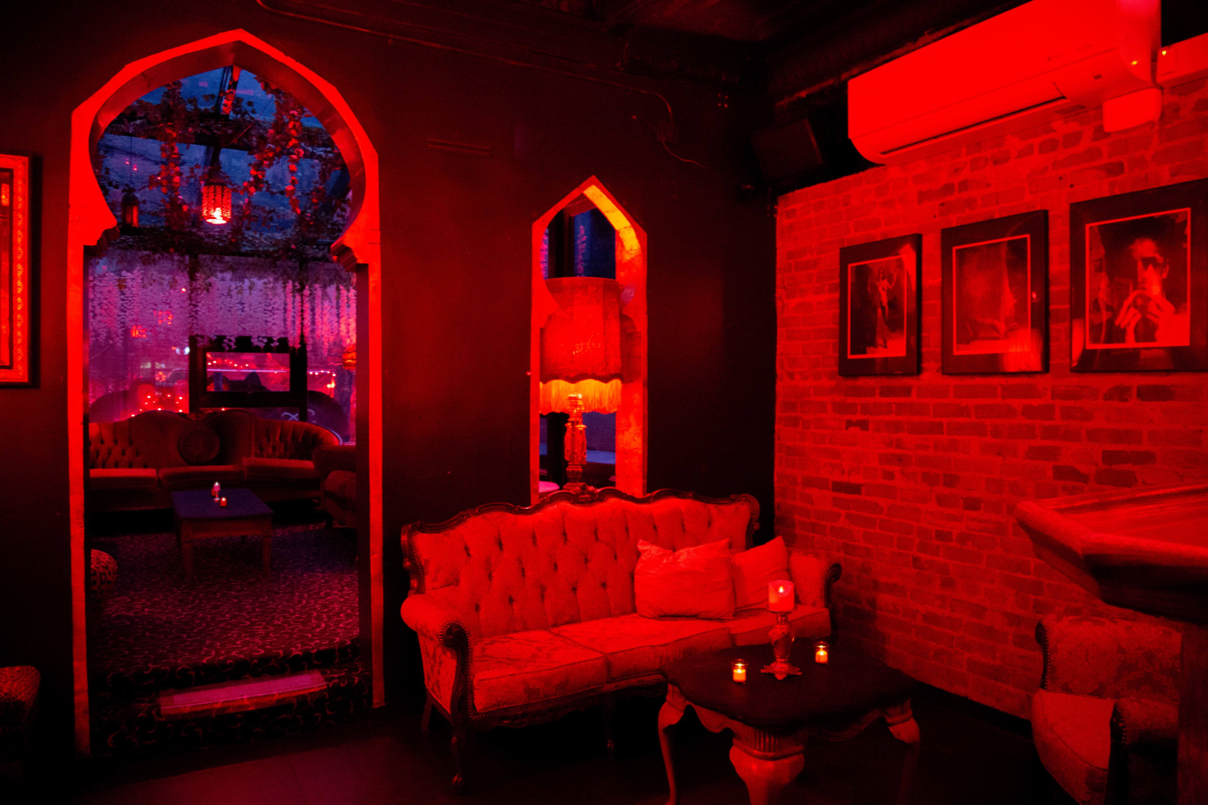 A dimly lit lounge area featuring ornate seating, red ambient lighting, and decorative walls with framed photographs.
